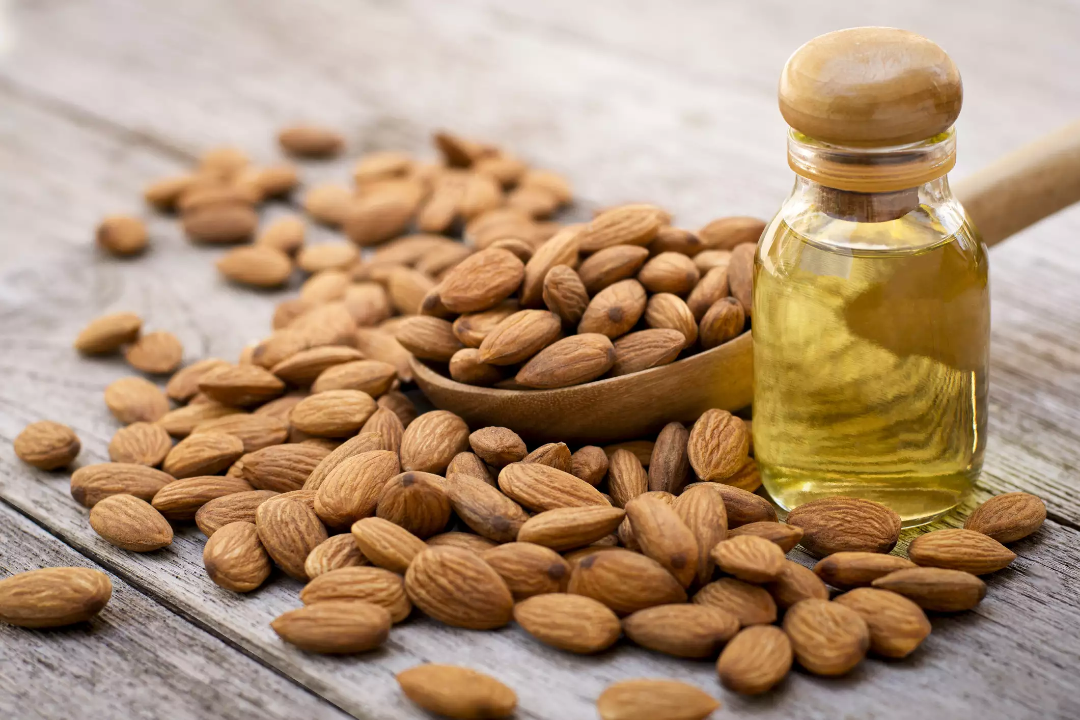 Closeup almond oil in glass bottle and group of almond nuts in wooden spoon isolated on wood table background.