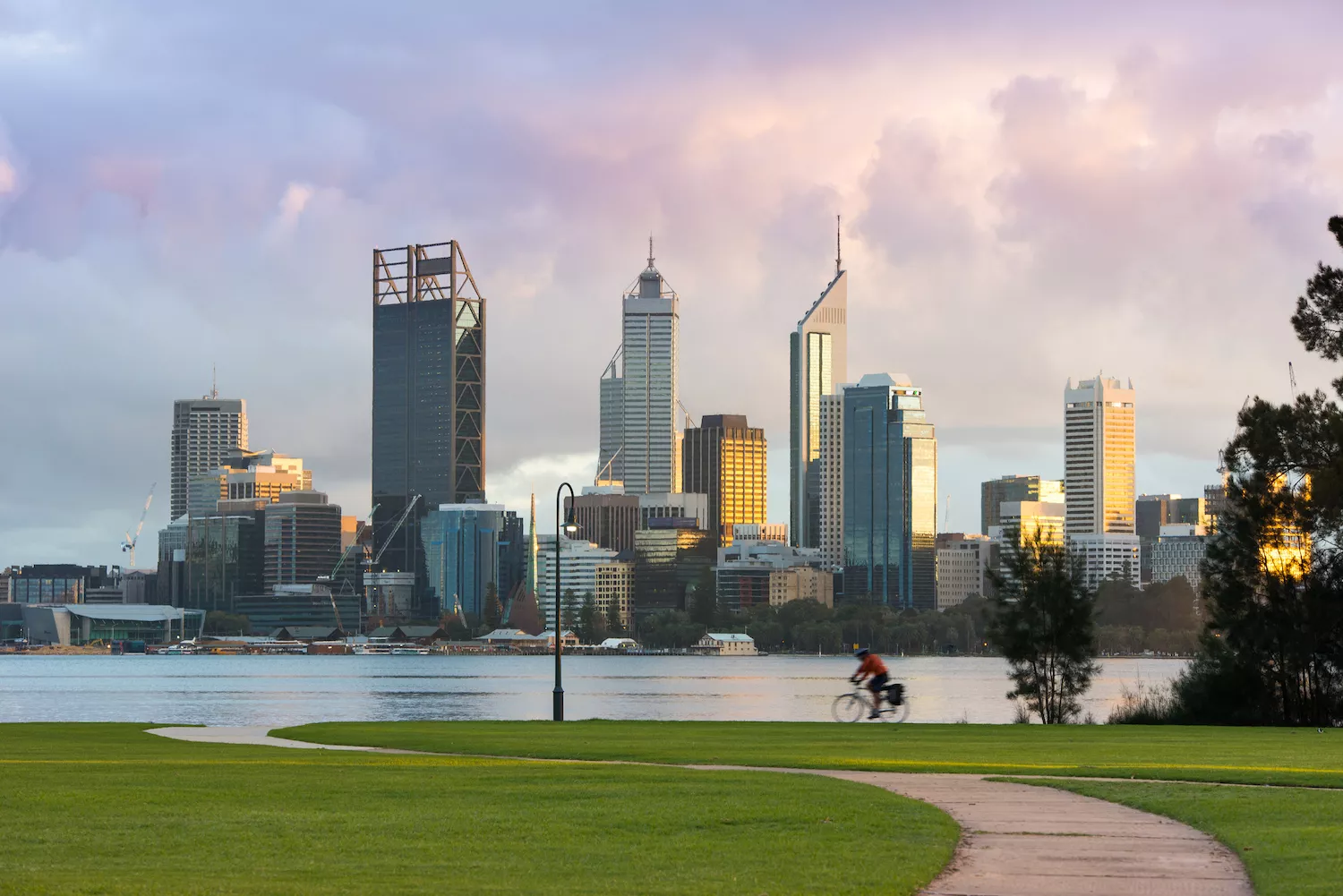 A cyclist pedals in front of the Perth skyline on a cloudy morning