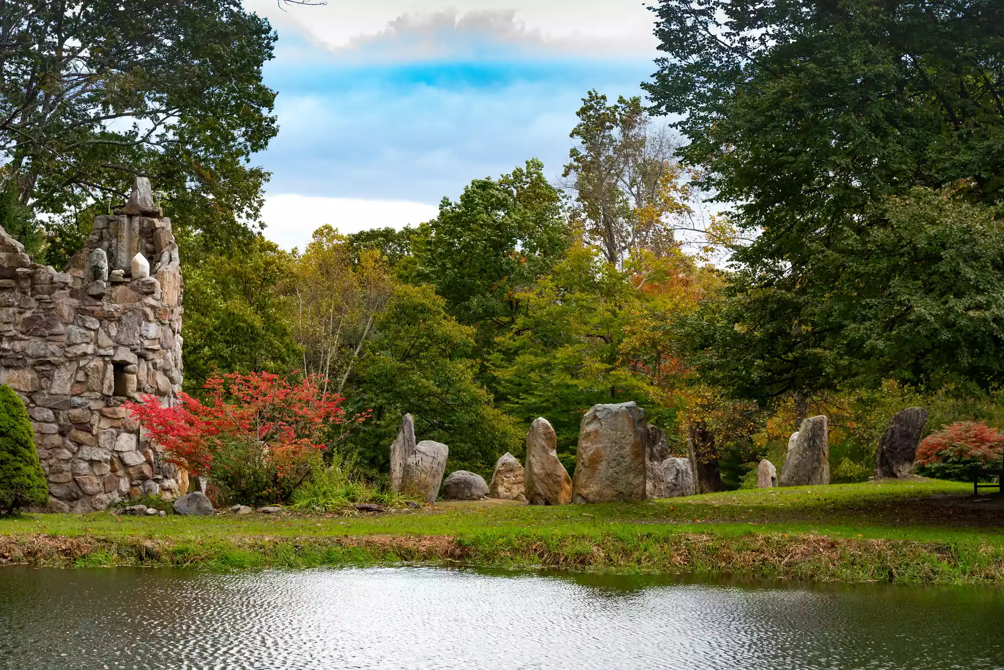 A stone bell tower and circle of stone structures with a pond in the foreground
