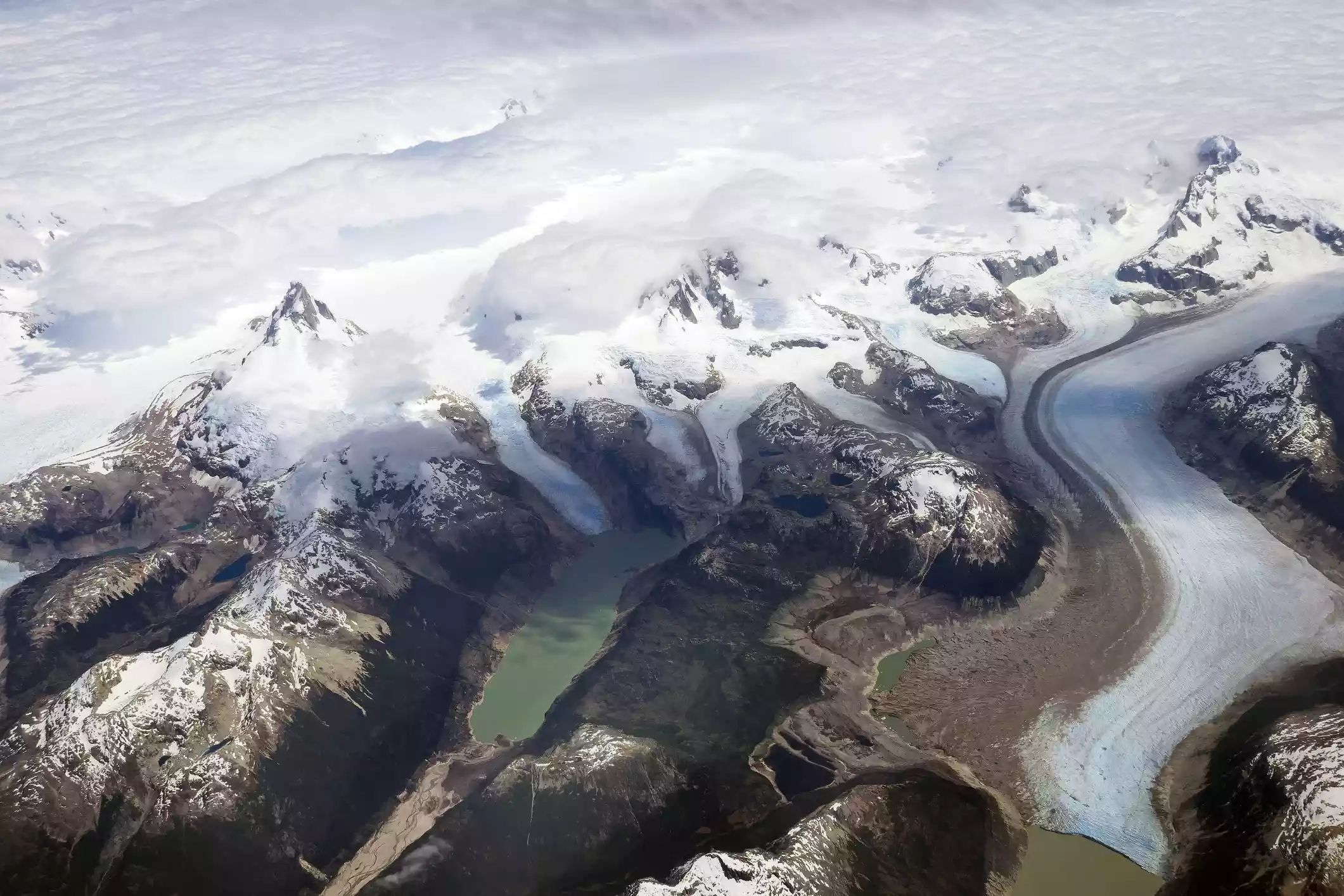 An aerial photo of a gray-green lake dammed by the arm of a large glacier