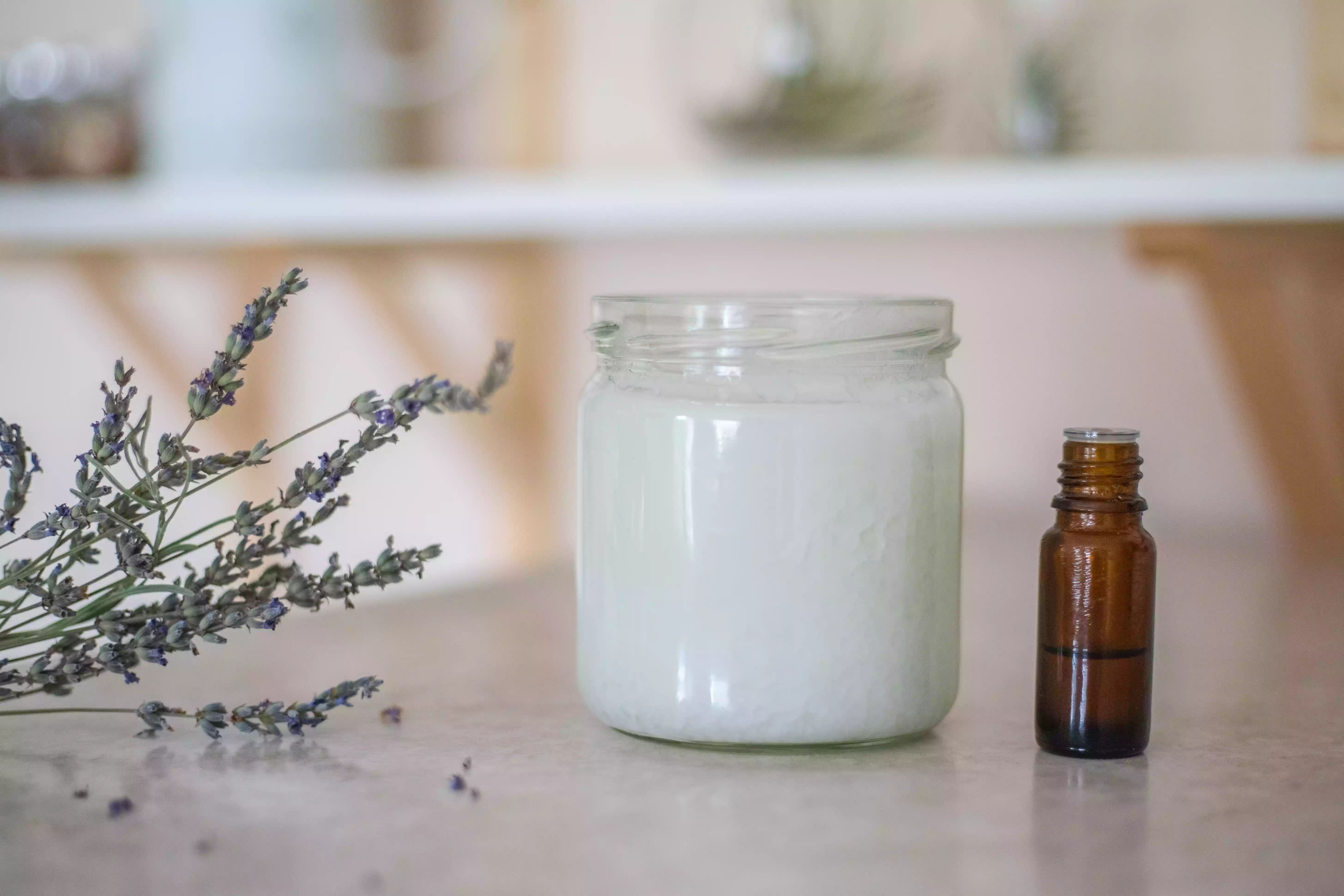 a glass jar of coconut oil next to lavender essential oil and a sprig of dried lavender flowers