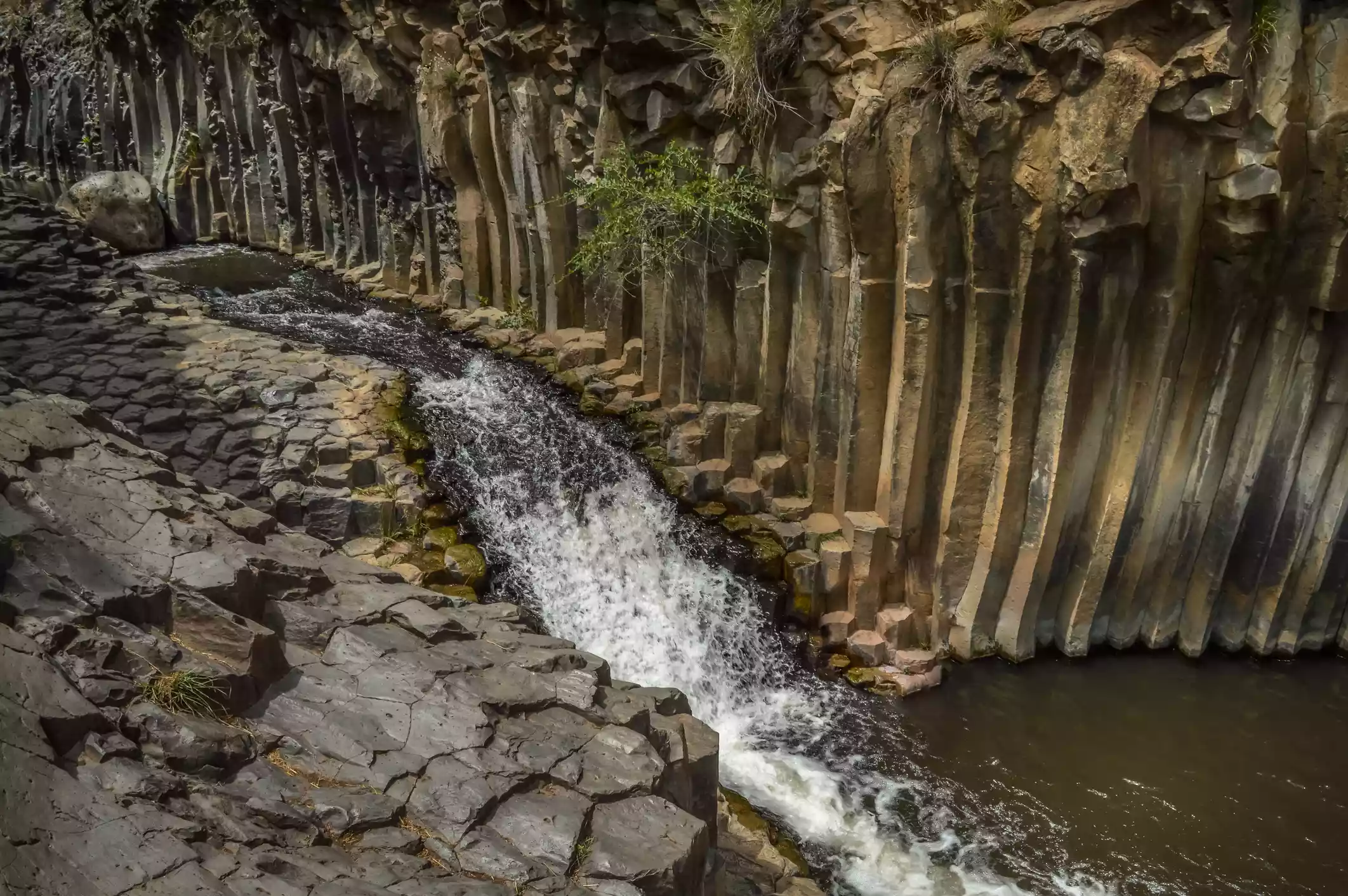 Waterfall cutting through hexagon basalt rock formation into pool
