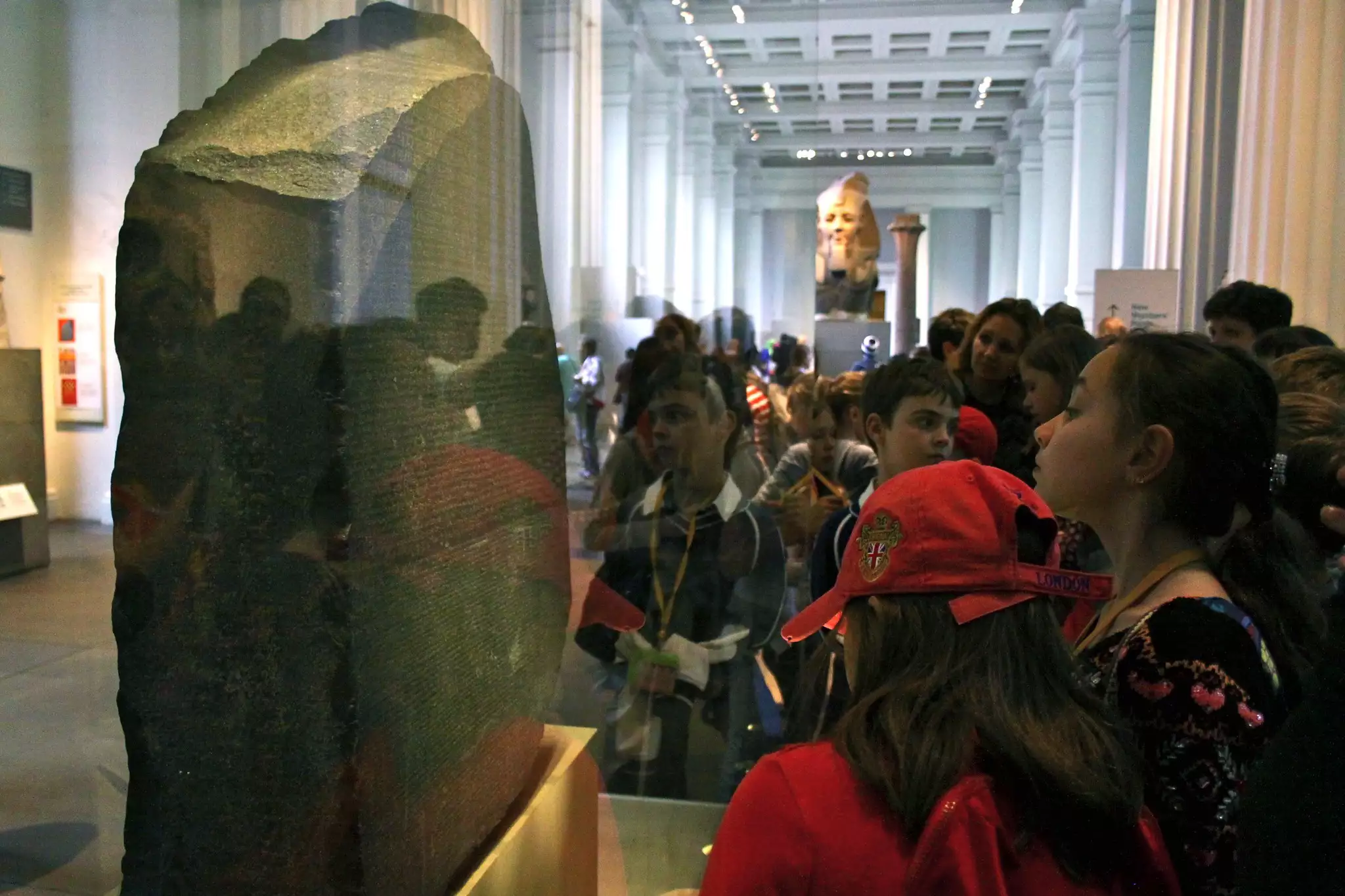 Schoolchildren gather around a display case featuring a stone slab covered in engravings