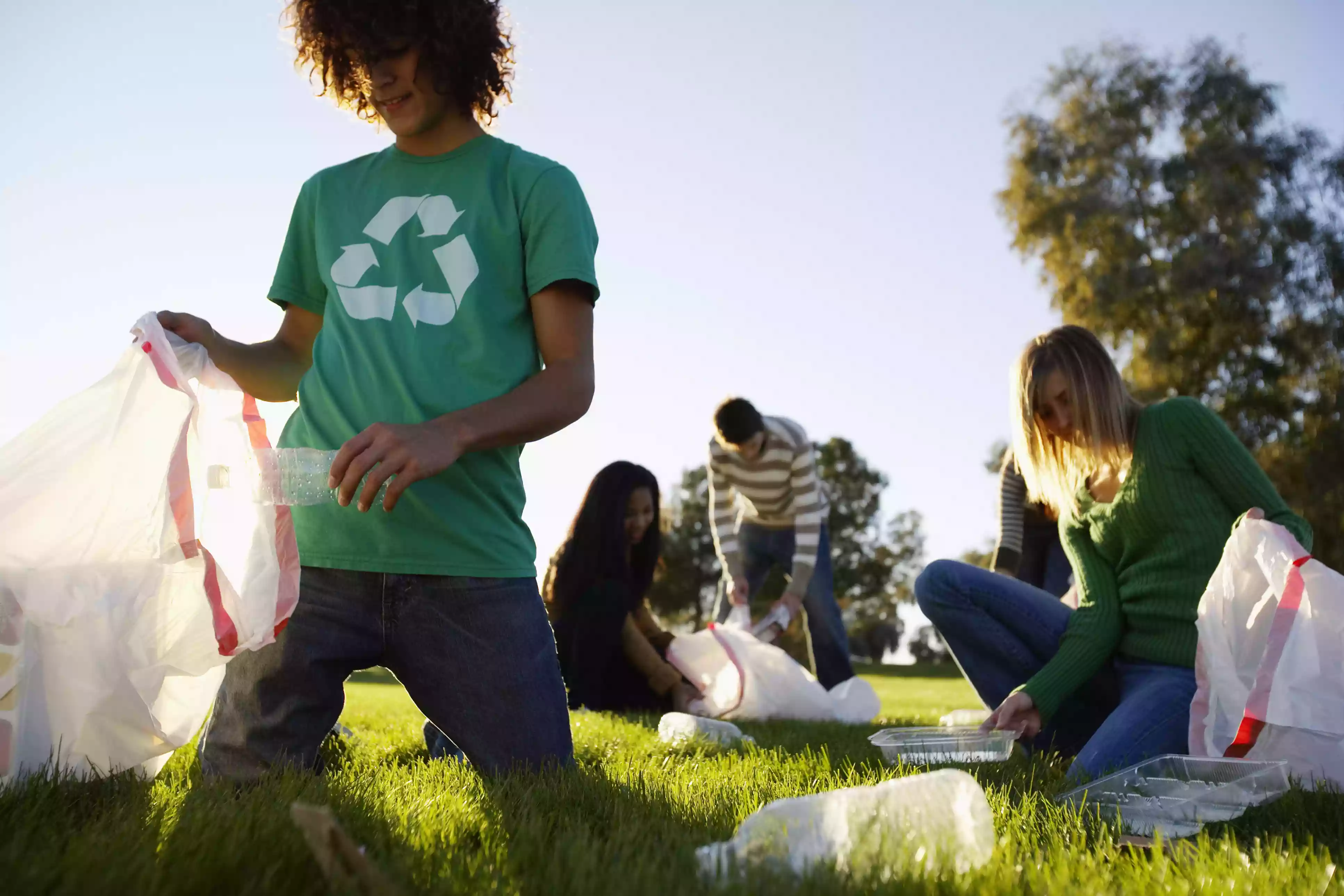 Young people picking up trash in a field on a sunny day.