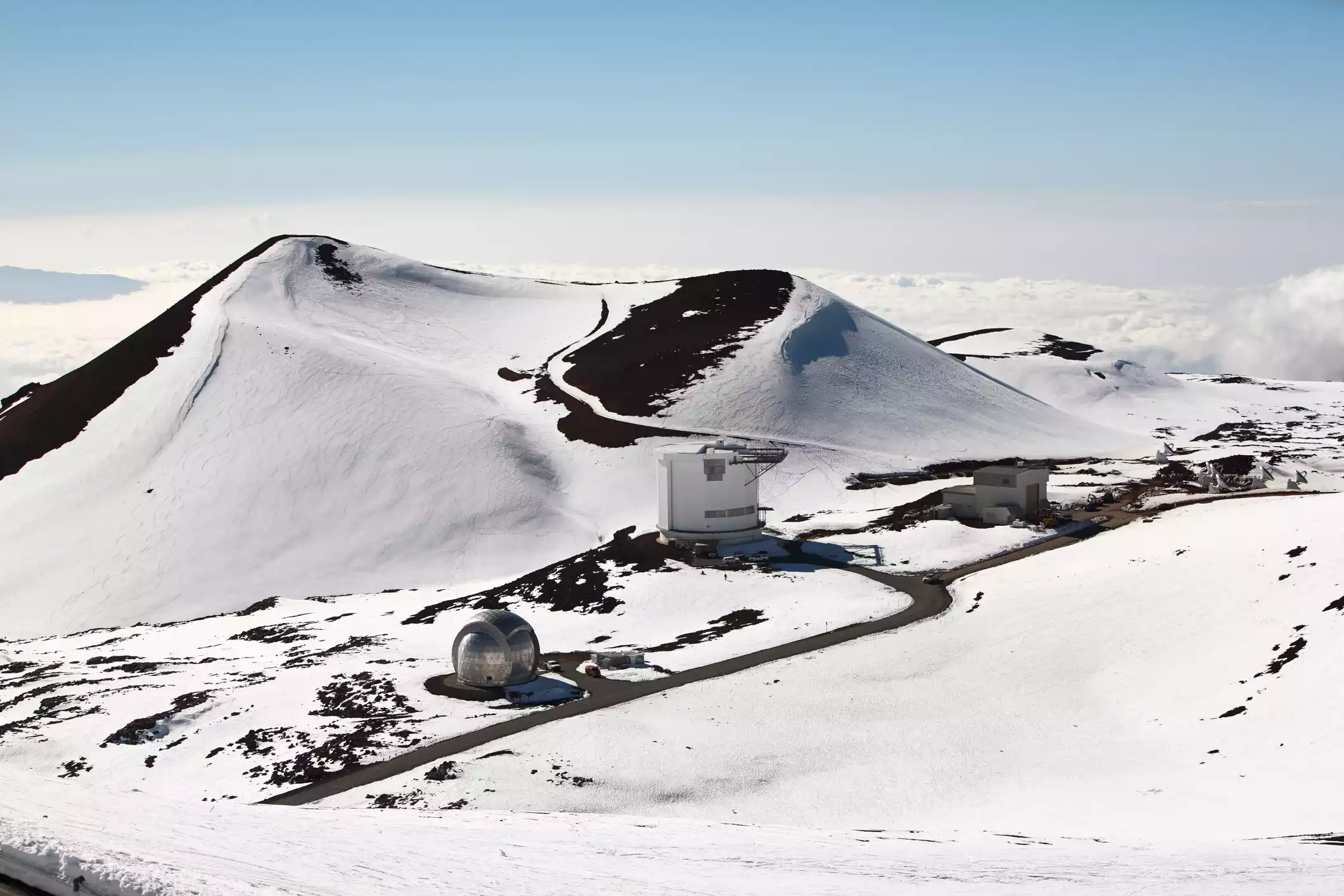 Mount Kea summit blanketed in white snow with some patches of brown dirt and light blue sky