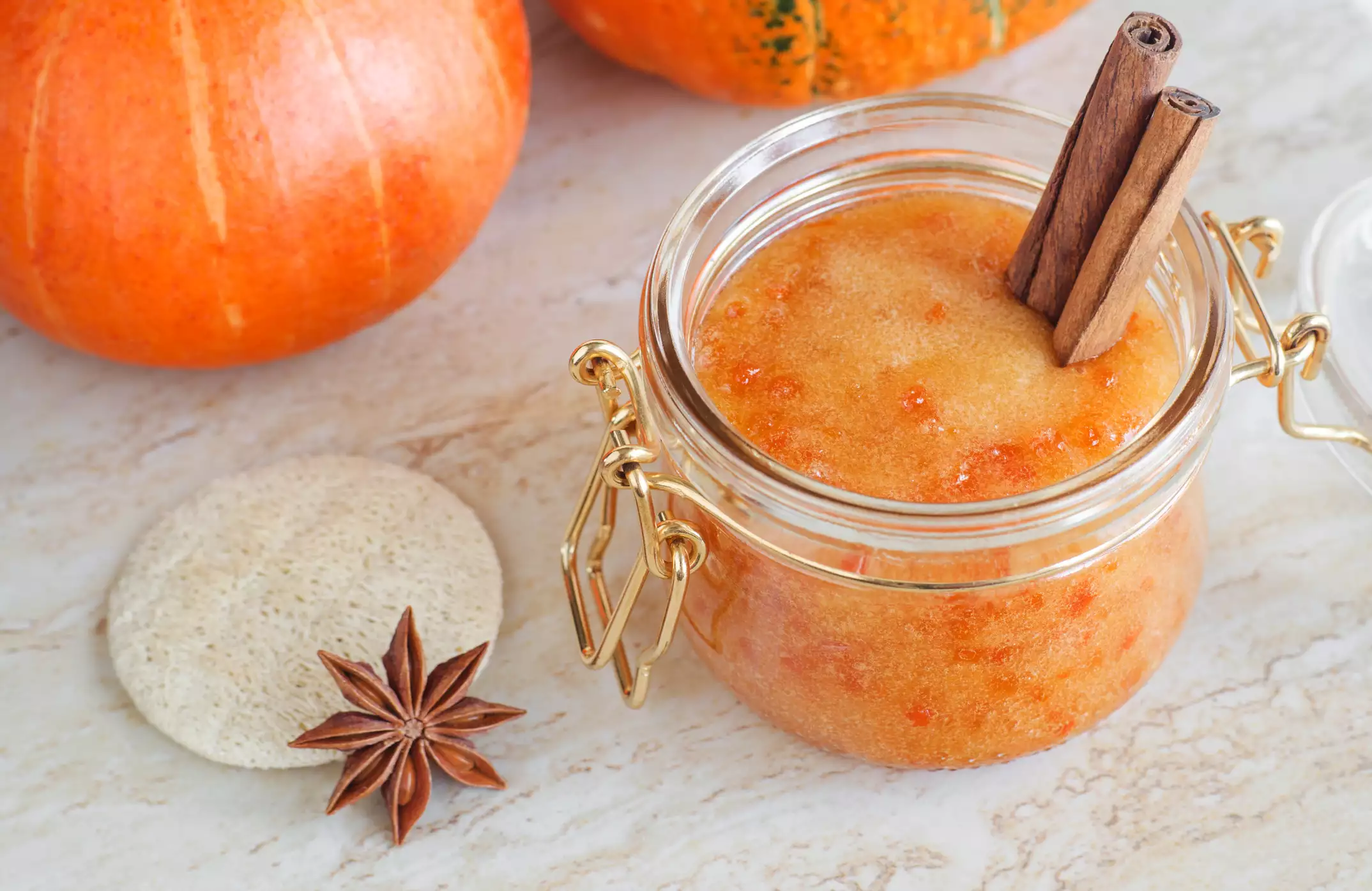Pumpkin scrub in a glass jar with a loofah pad and cinnamon sticks.
