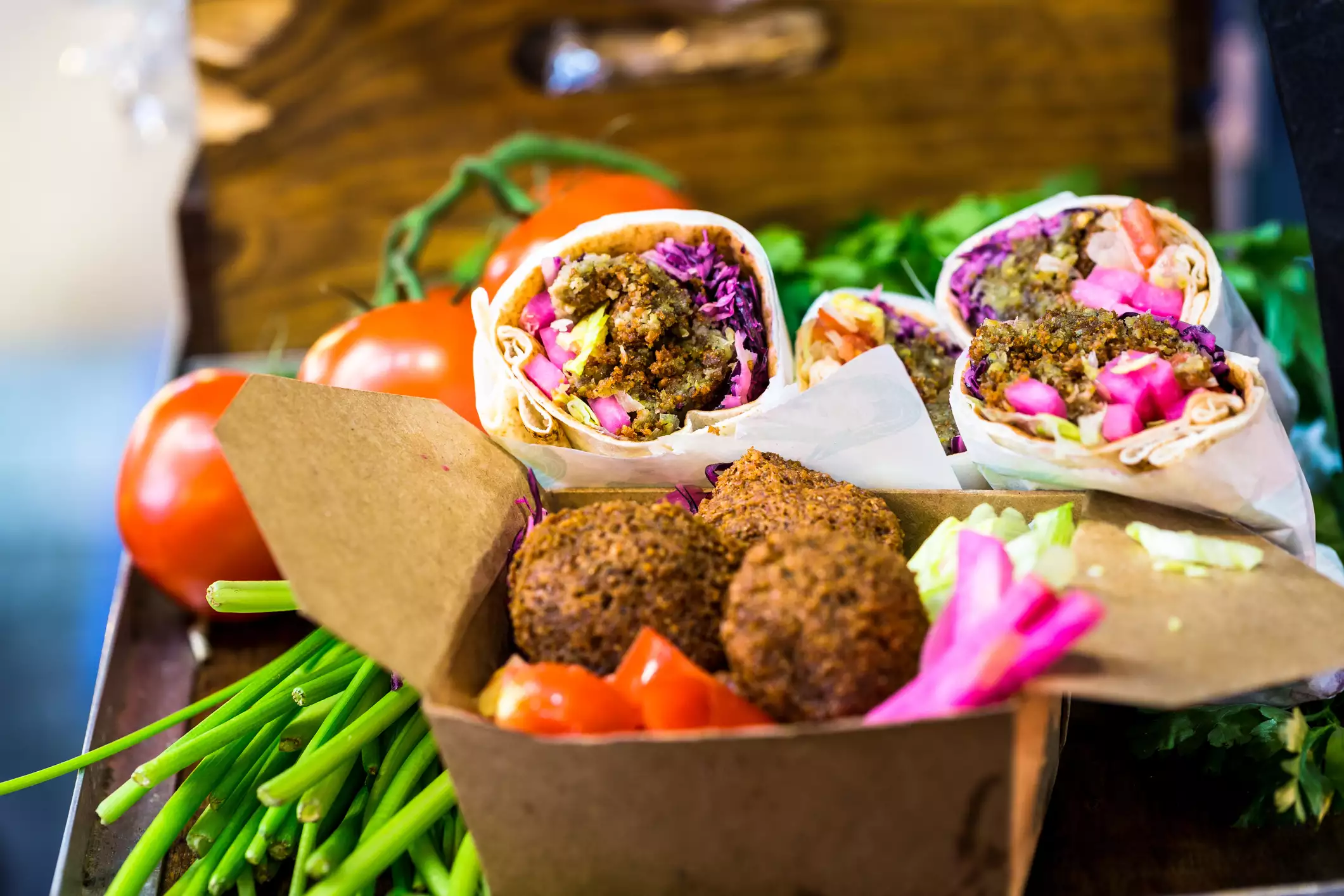 Close up image of boxes of vegetarian food for sale on a market stall at Borough Market, a famous food market in central London, UK. In the foreground a brown cardboard box is attractively filled with falafel balls, red cabbage and tomato, beyond this are wraps filled with falafel, tomato and red cabbage.