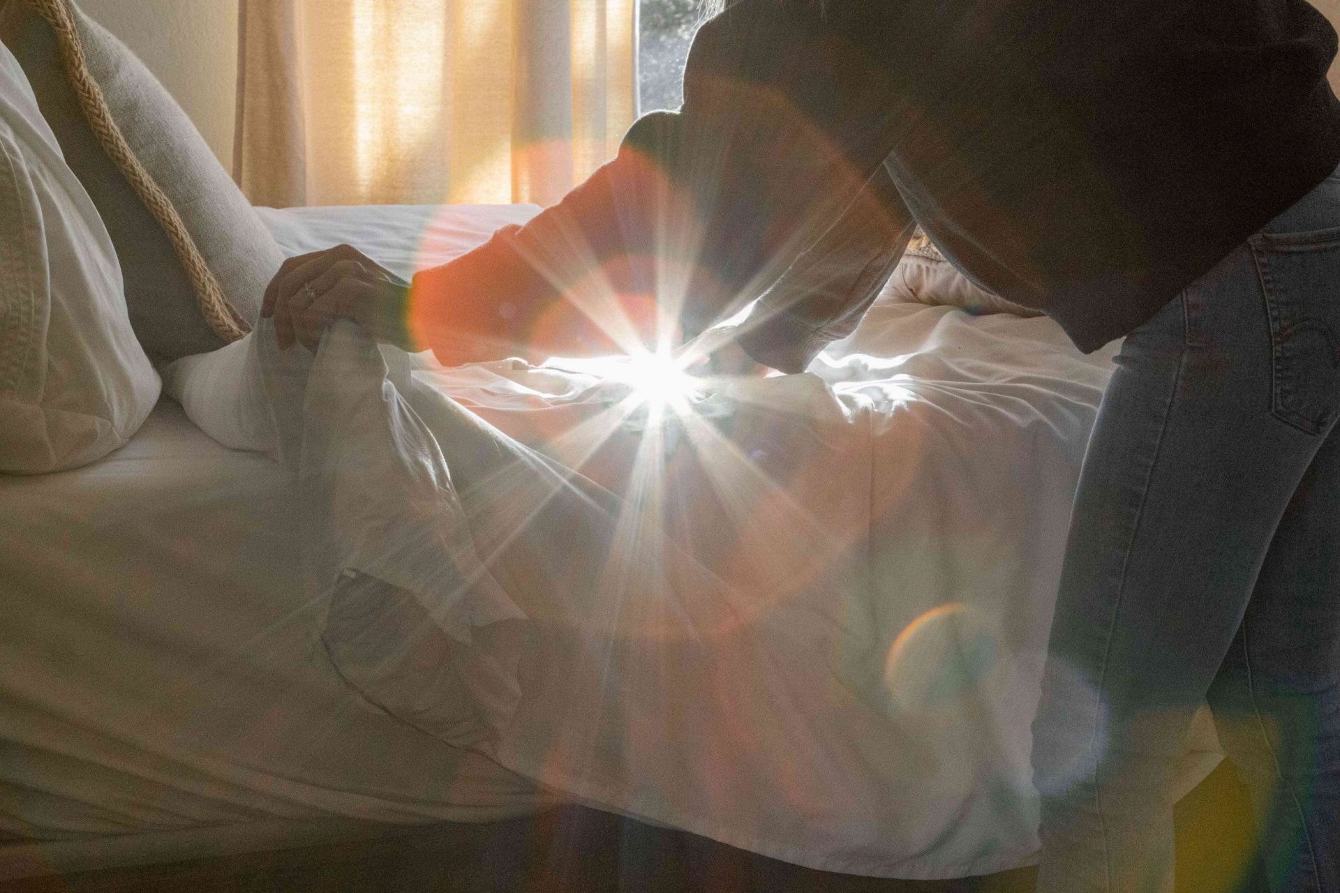 una persona hace la cama mientras la luz del sol que entra por la ventana emite un rayo de luz en la cámara