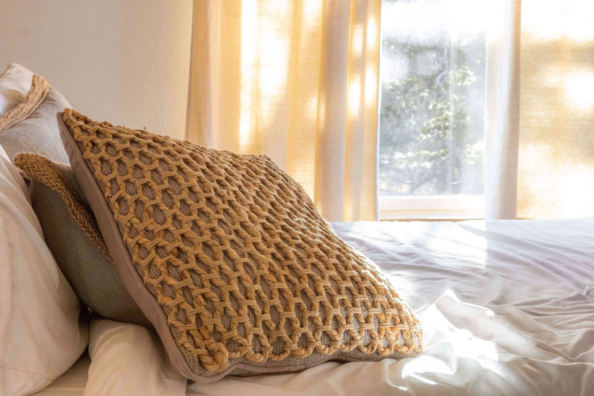 una cama bien hecha con almohadas con textura en primer plano y una ventana soleada al fondo