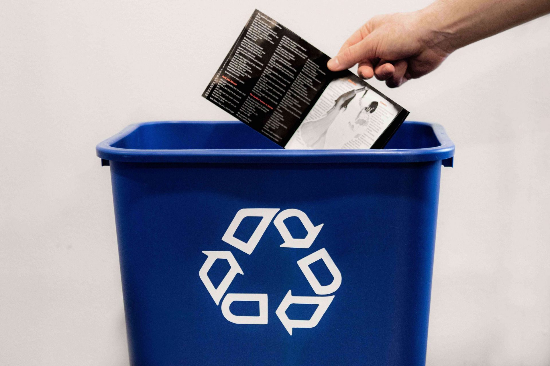 la mano deja caer el papel de la caja del CD en el contenedor azul de reciclaje