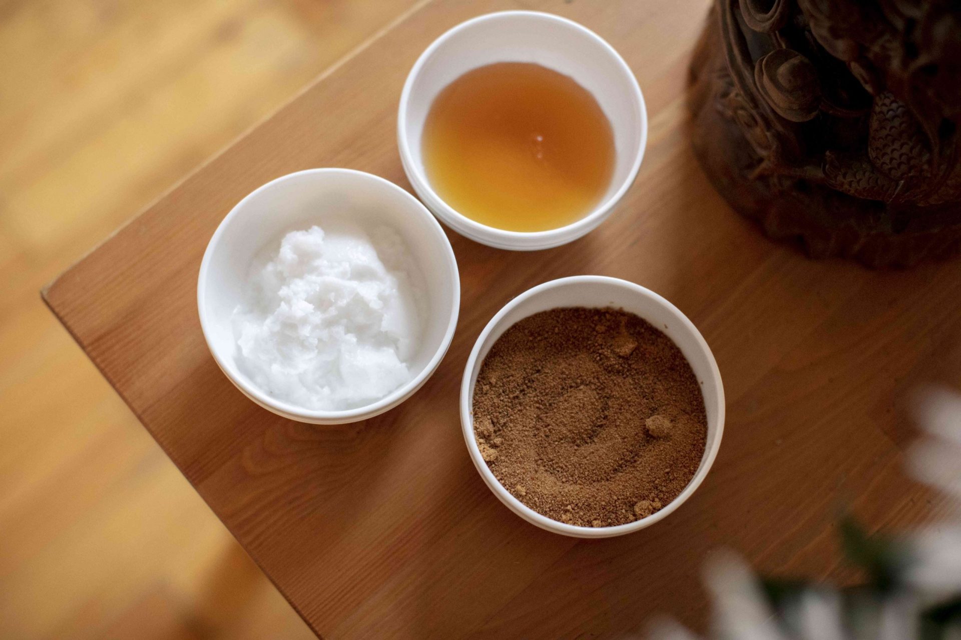 azúcar de coco, aceite de coco y miel en cuencos de cerámica blanca sobre una mesa de madera para un exfoliante labial diy