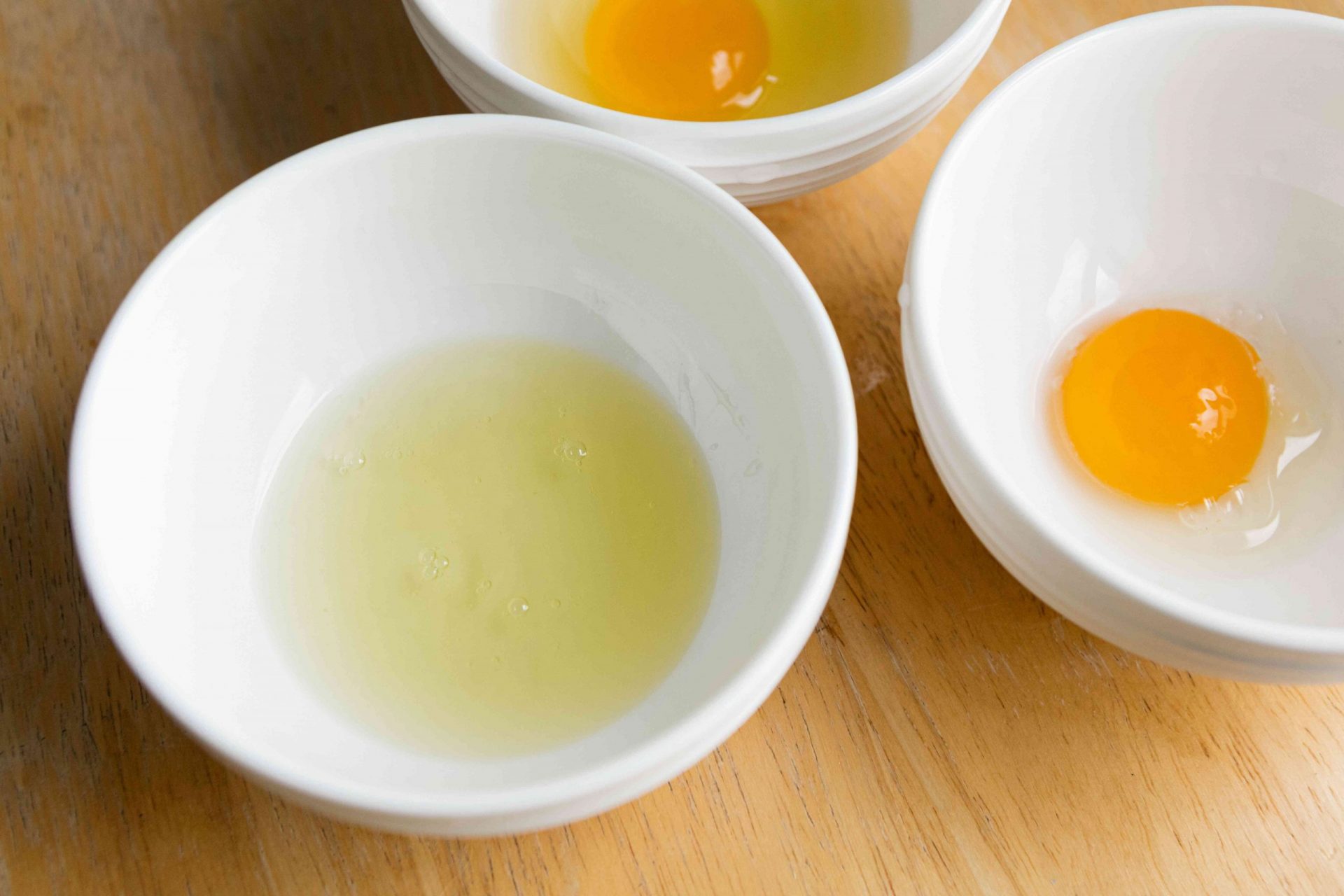 tres cuencos blancos con tres huevos crudos: la clara, la yema y el conjunto