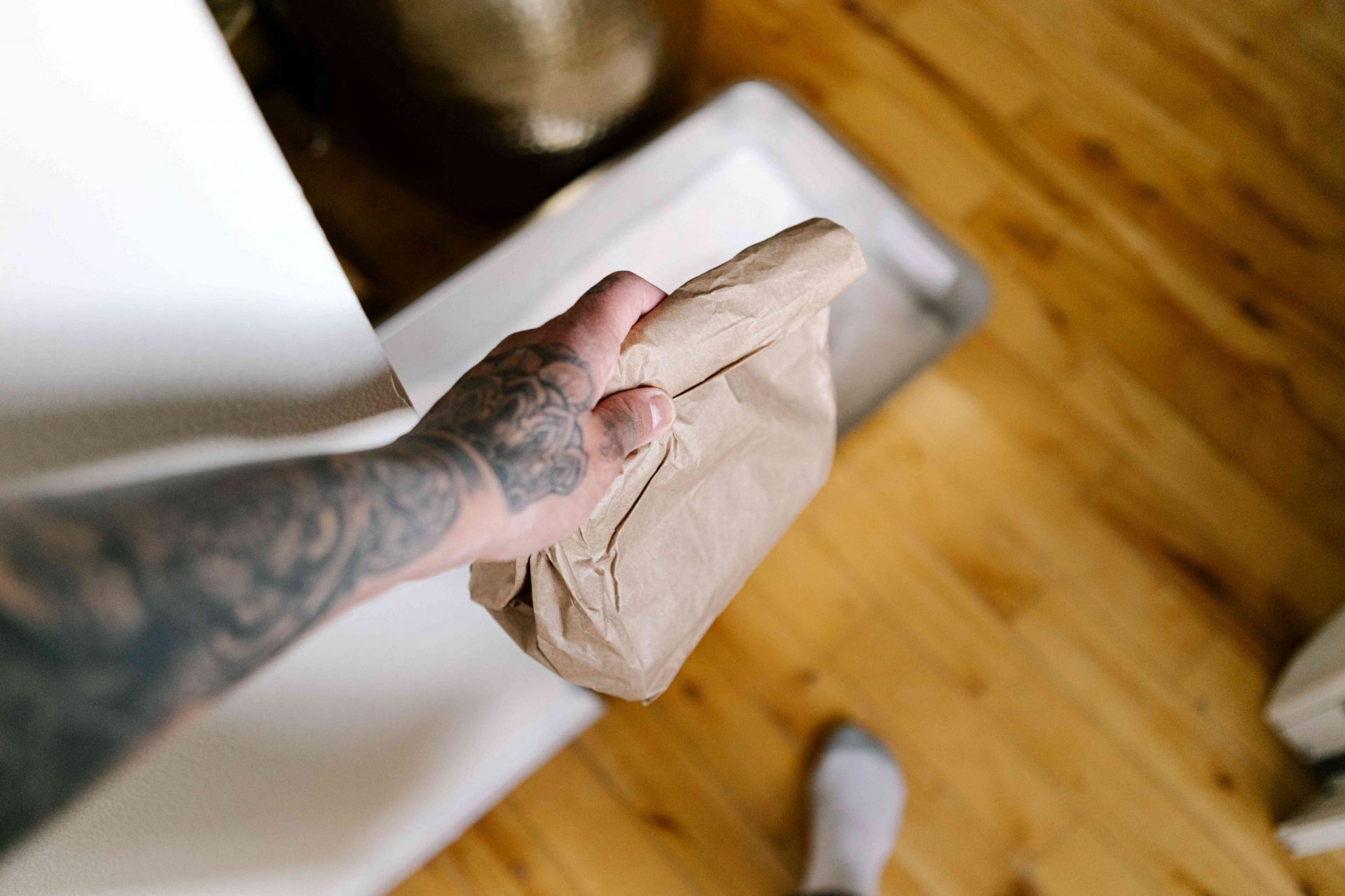 una mano tatuada lleva una bolsa de papel marrón con residuos de gato más allá de la caja de arena
