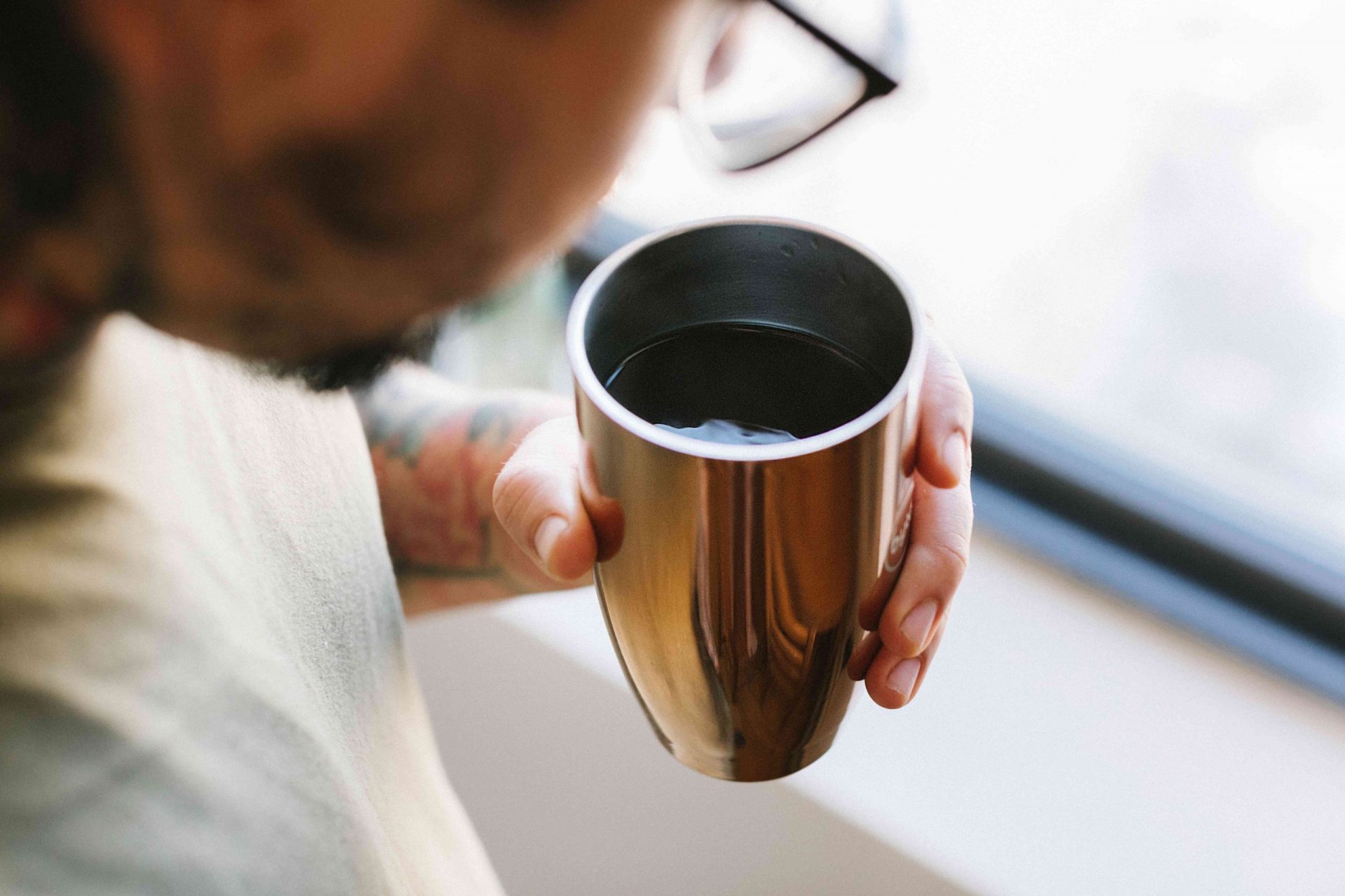 persona con gafas mira una taza de café caliente en un vaso reutilizable