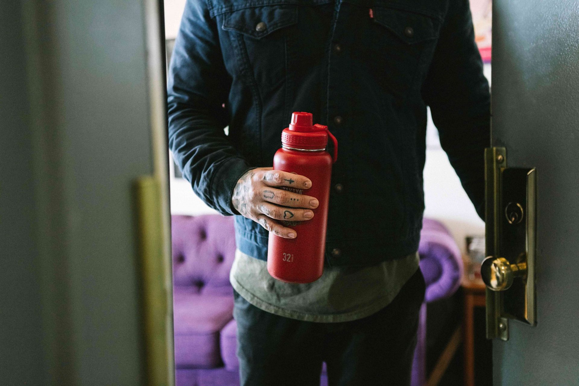 persona abriendo la puerta del apartamento con un termo rojo reutilizable en la mano