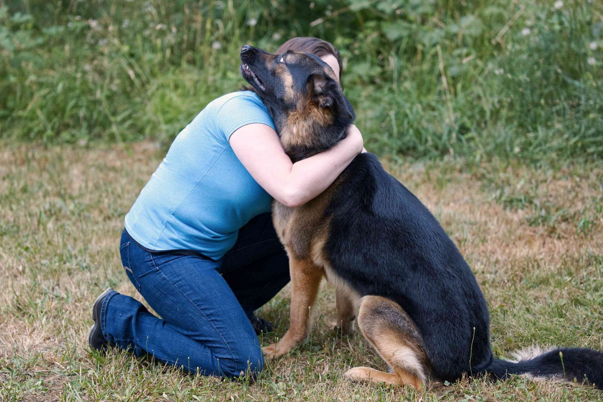 una mujer se arrodilla en la hierba para dar a un pastor alemán un abrazo que no quiere