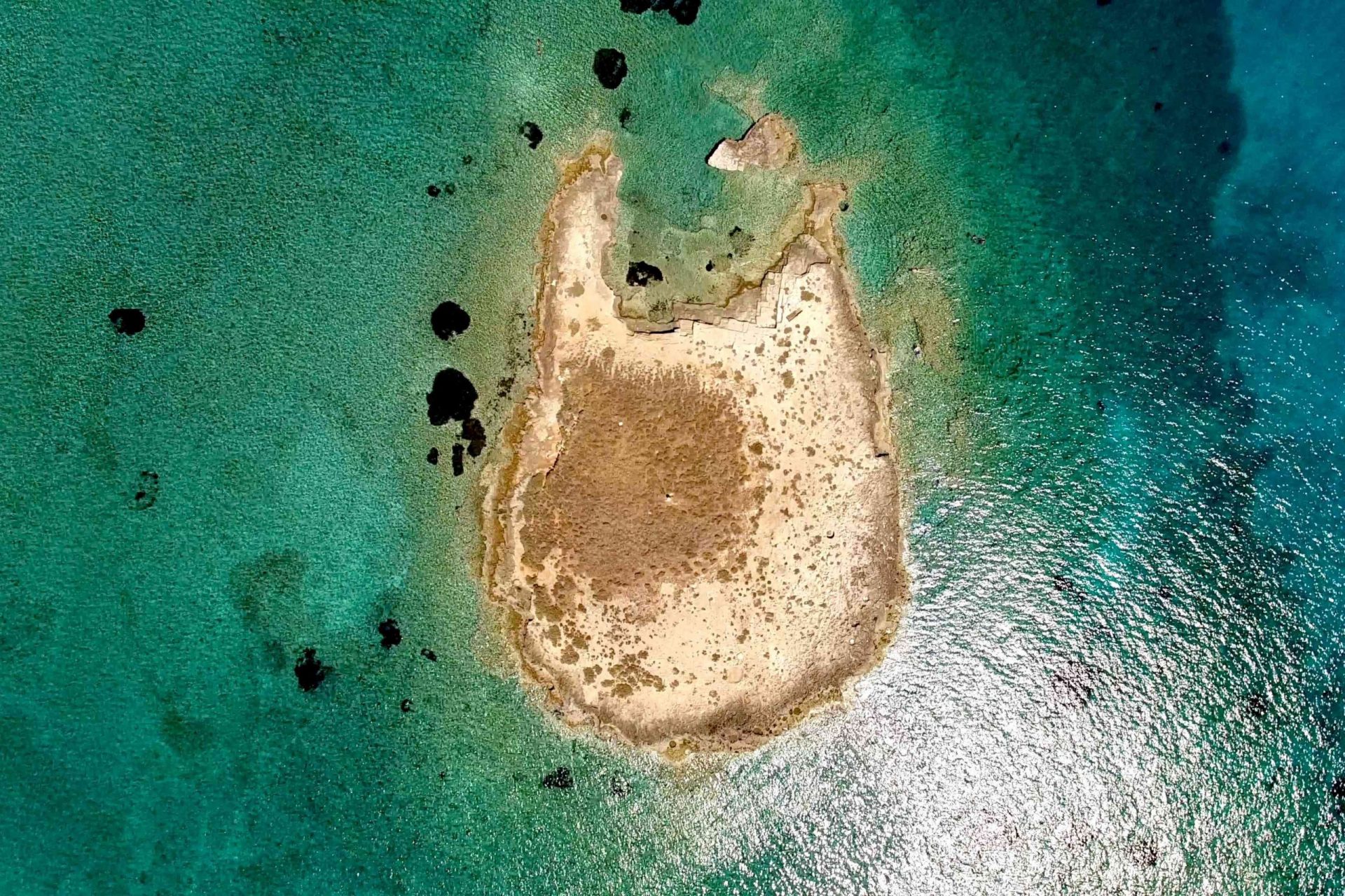 Toma de un dron de una isla y del mar que contiene una ciudad sumergida