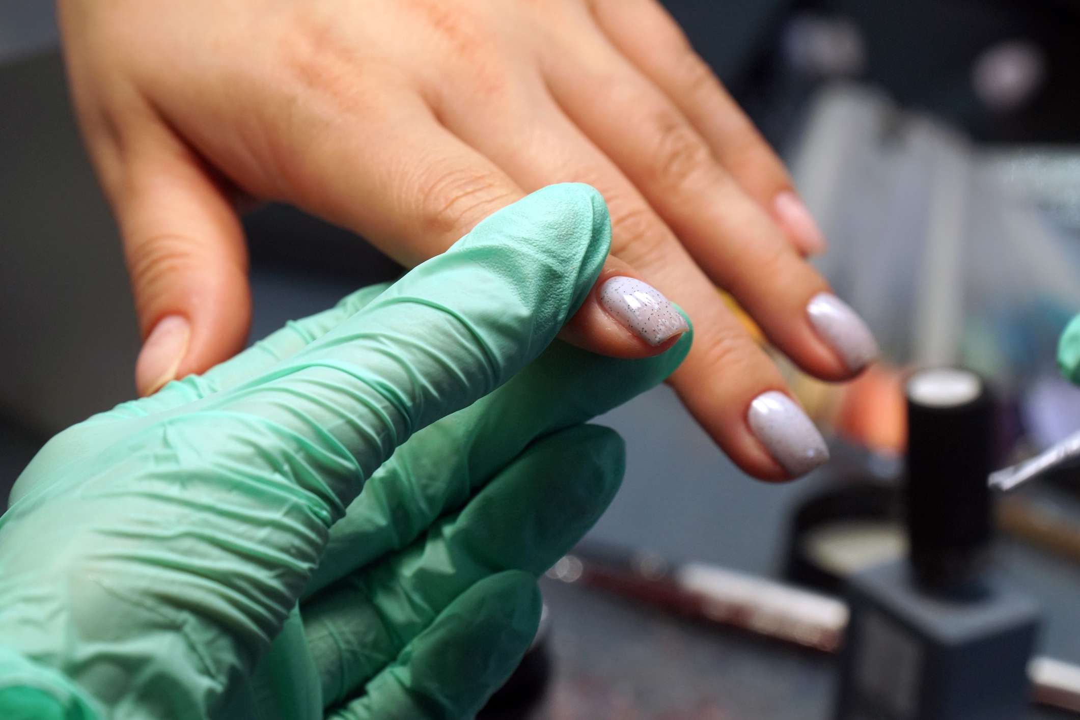 Mano con guante sujetando las uñas recién pintadas