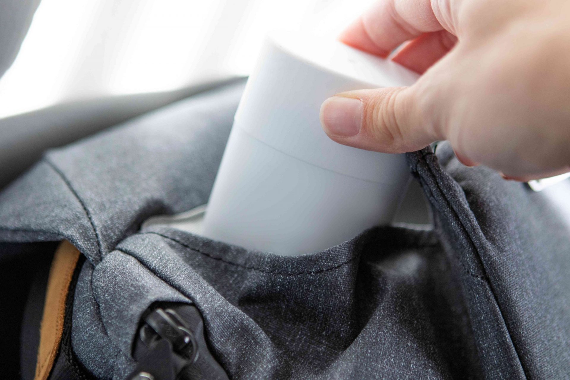 la mano coloca el desodorante en la mochila gris para poder reaplicarlo más tarde en el día