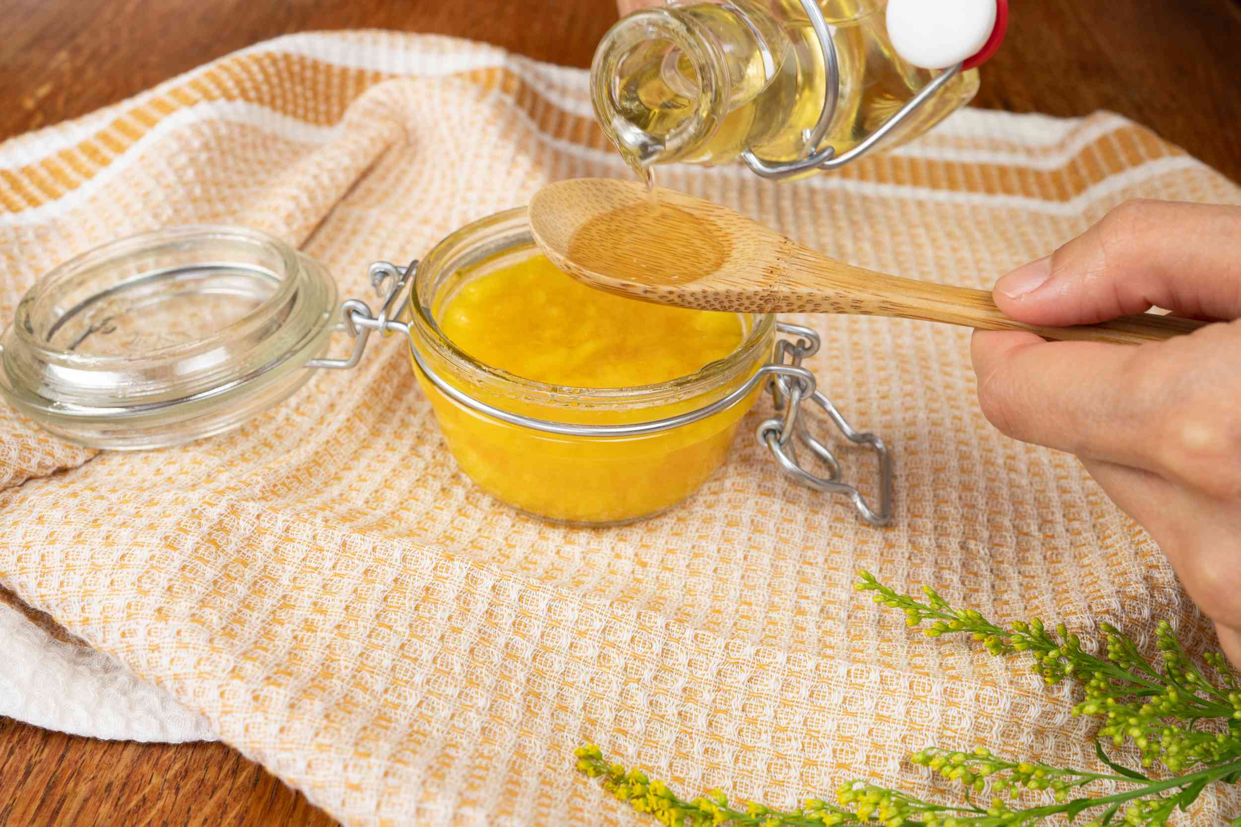 la miel se vierte en una cuchara de madera para hacer una mascarilla facial casera de mango en un tarro de cristal