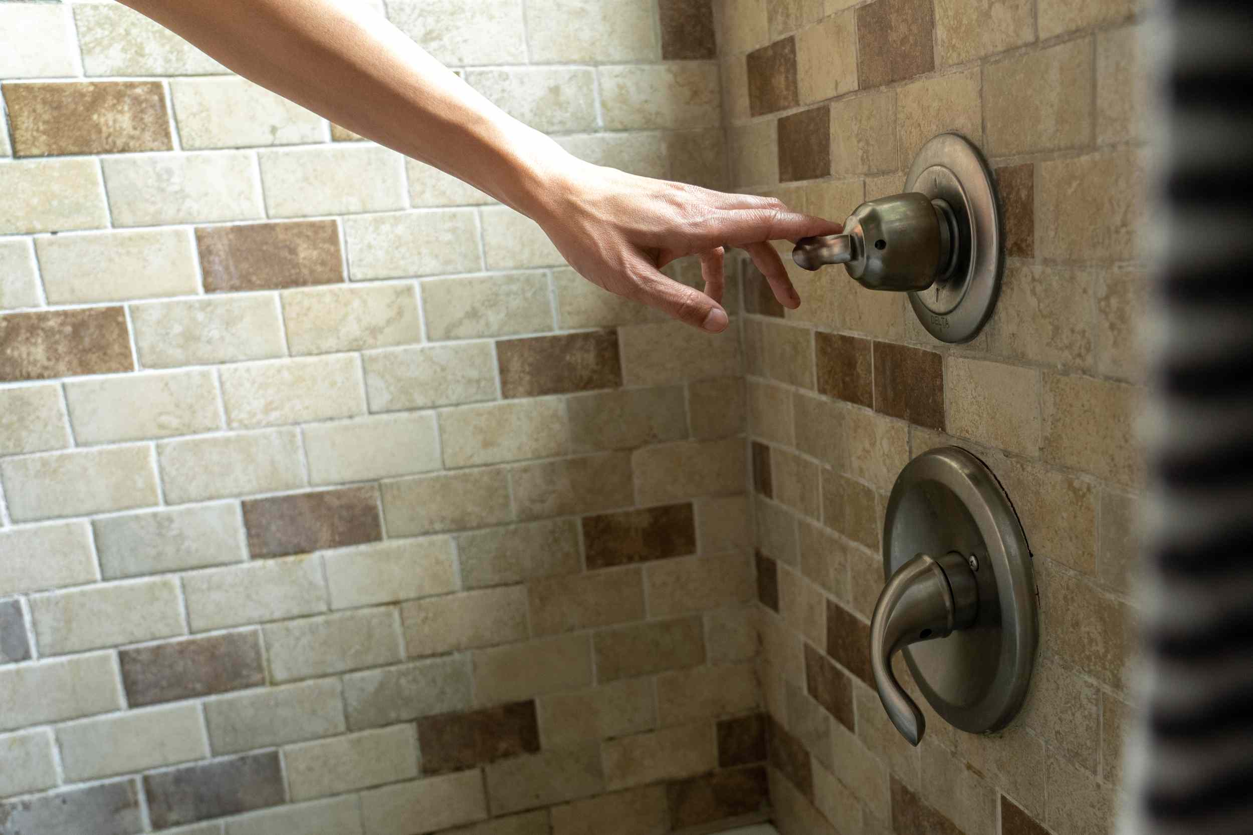 la mano se extiende para bajar la temperatura del agua en la ducha