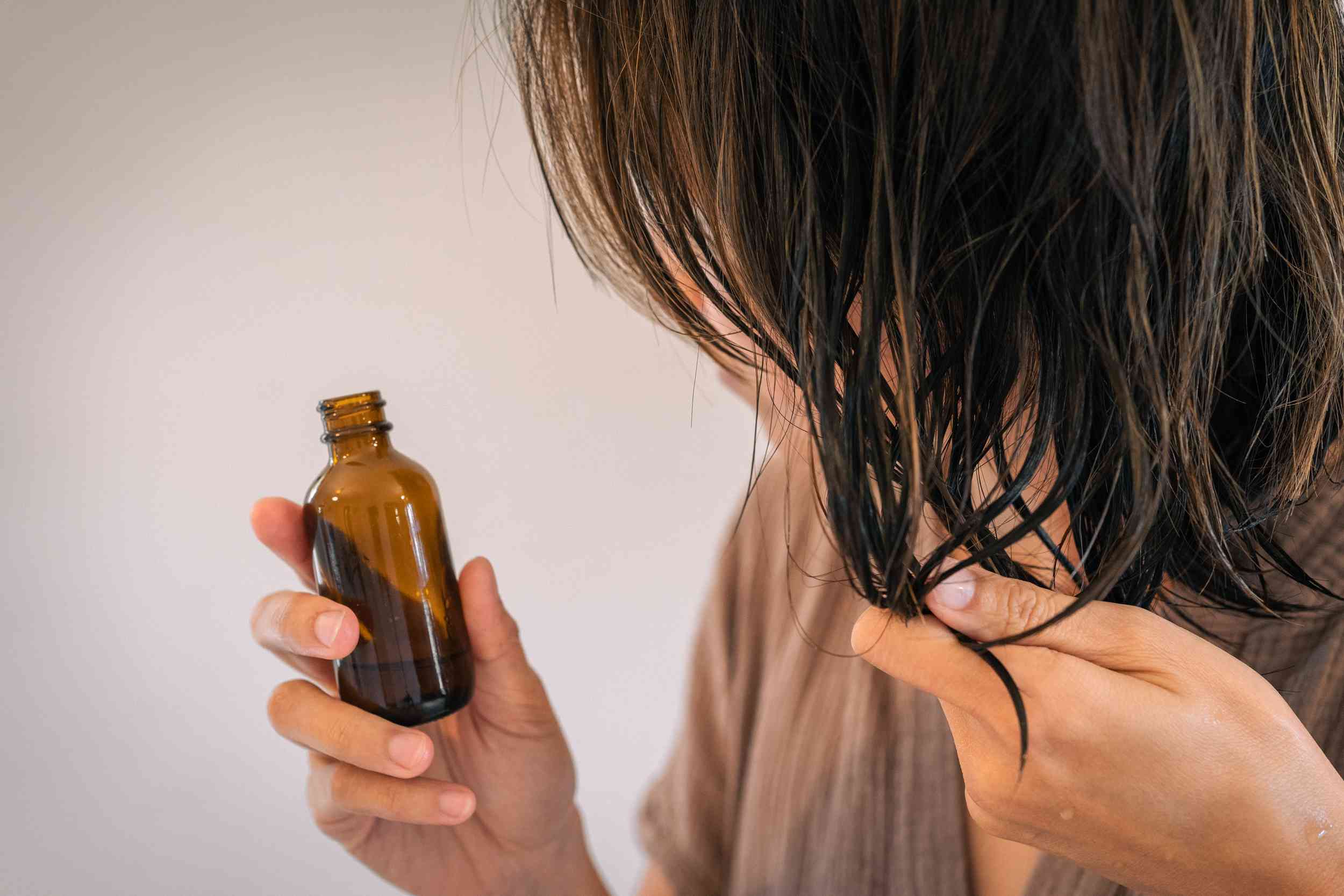 una persona exprime aceite en las puntas del pelo desde una botella de cristal marrón