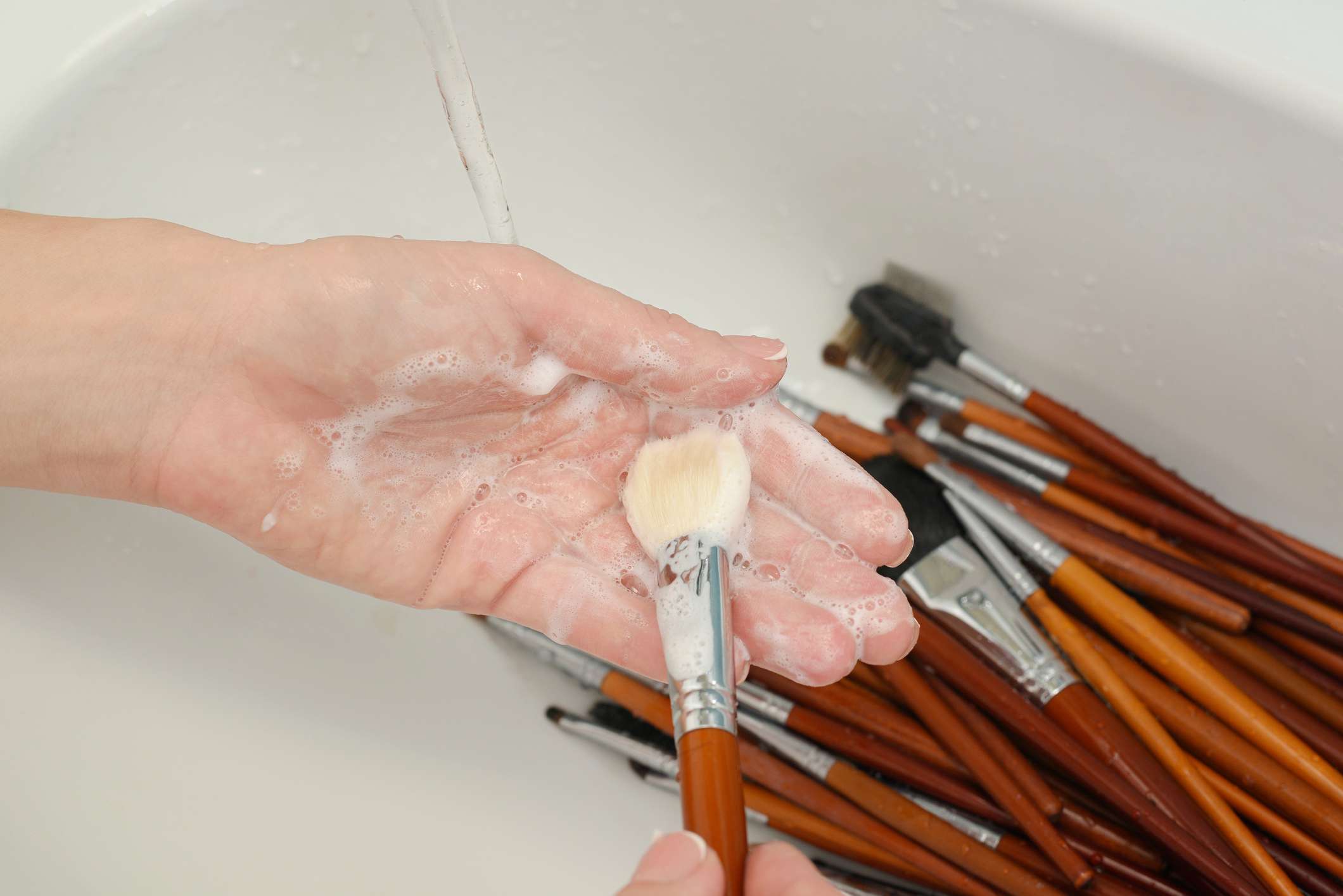 Persona lavando la brocha de maquillaje con jabón en la mano sobre el fregadero