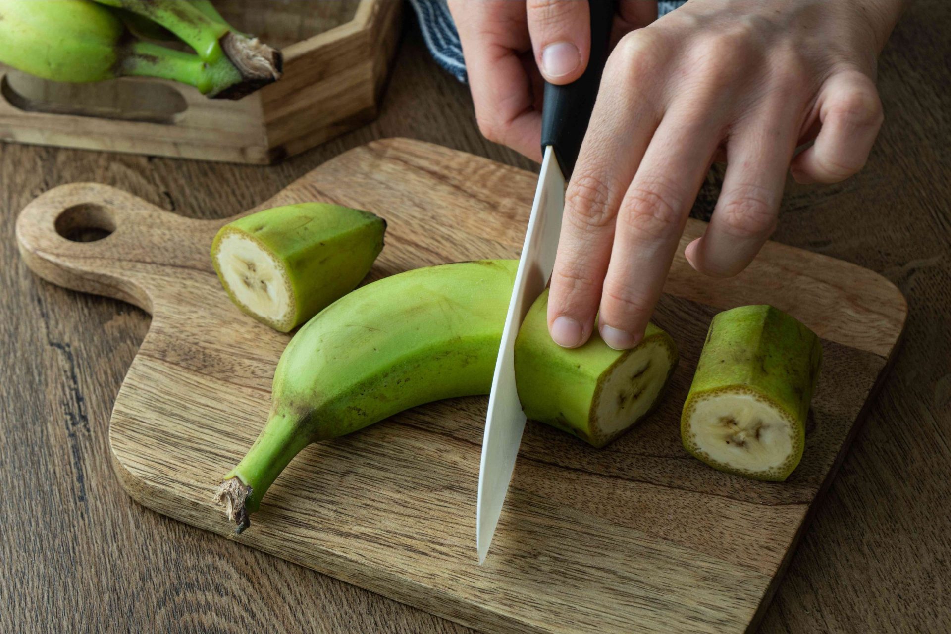 manos cortando plátano verde sobre una tabla de madera
