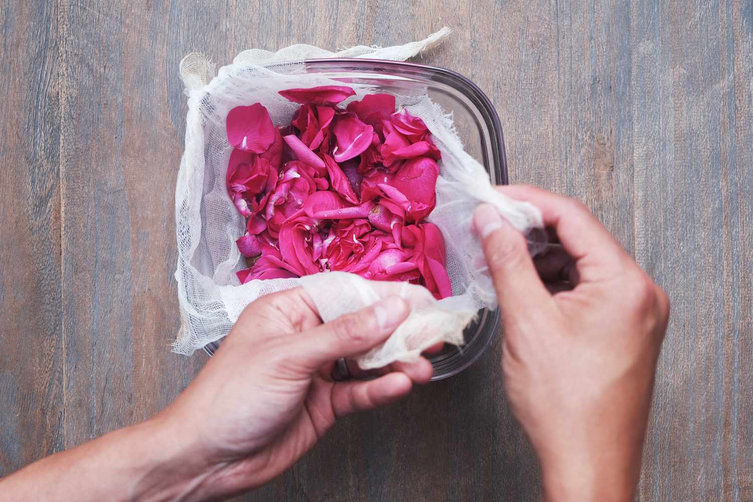 las manos cogen una estopilla forrada alrededor de un cuenco de cristal lleno de pétalos de rosa frescos
