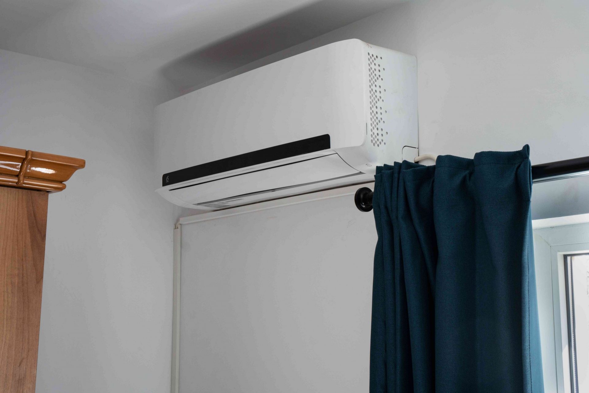 Imagen de una unidad doméstica de aire acondicionado dividida en una pared blanca cerca de la ventana con una cortina colgando