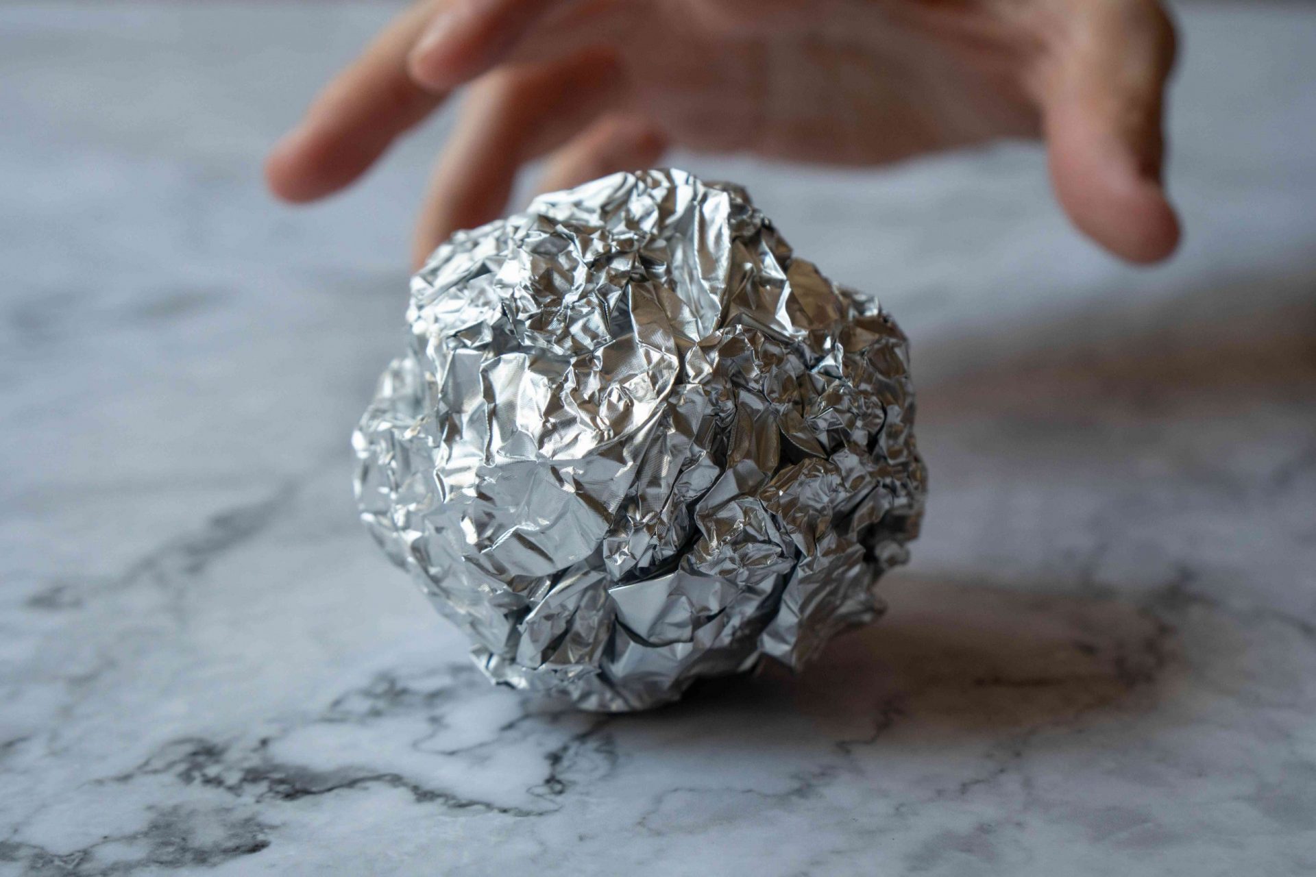 la mano busca una bola de papel de aluminio arrugado en la superficie del mármol