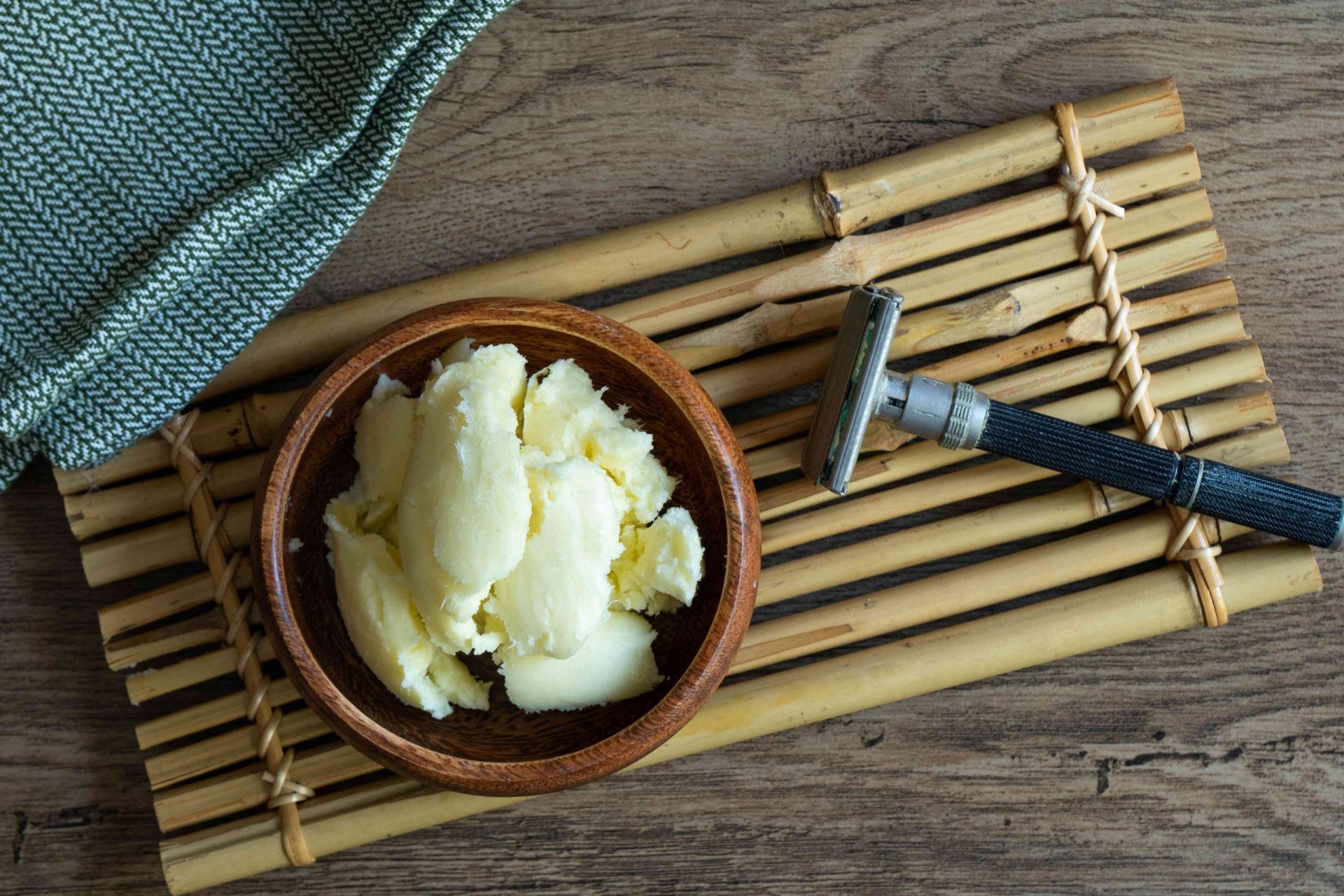 cuenco de madera de manteca de karité cruda con maquinilla de afeitar de metal en bandeja de bambú