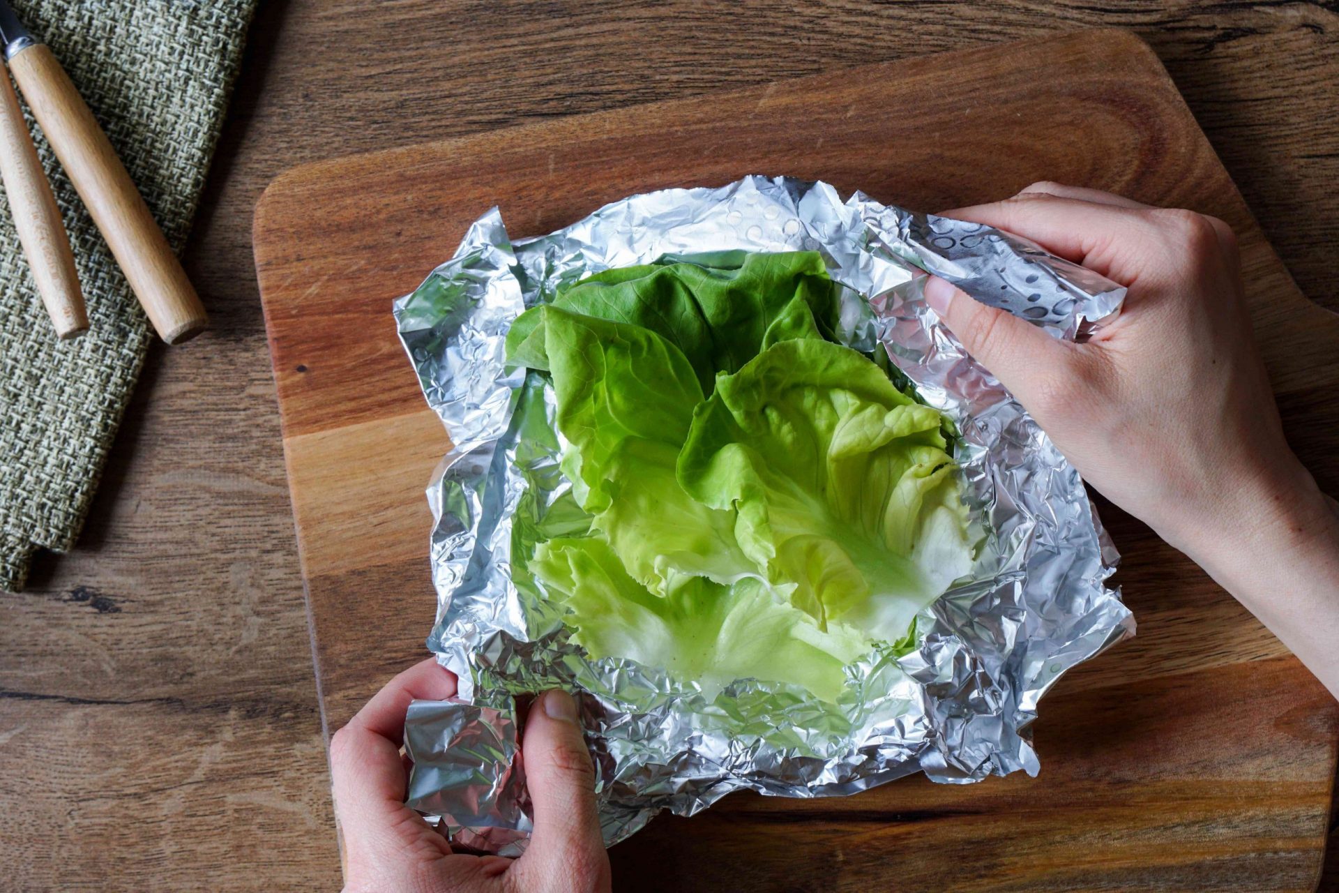 una mano envuelve las hojas de lechuga fresca en papel de aluminio para guardarlas