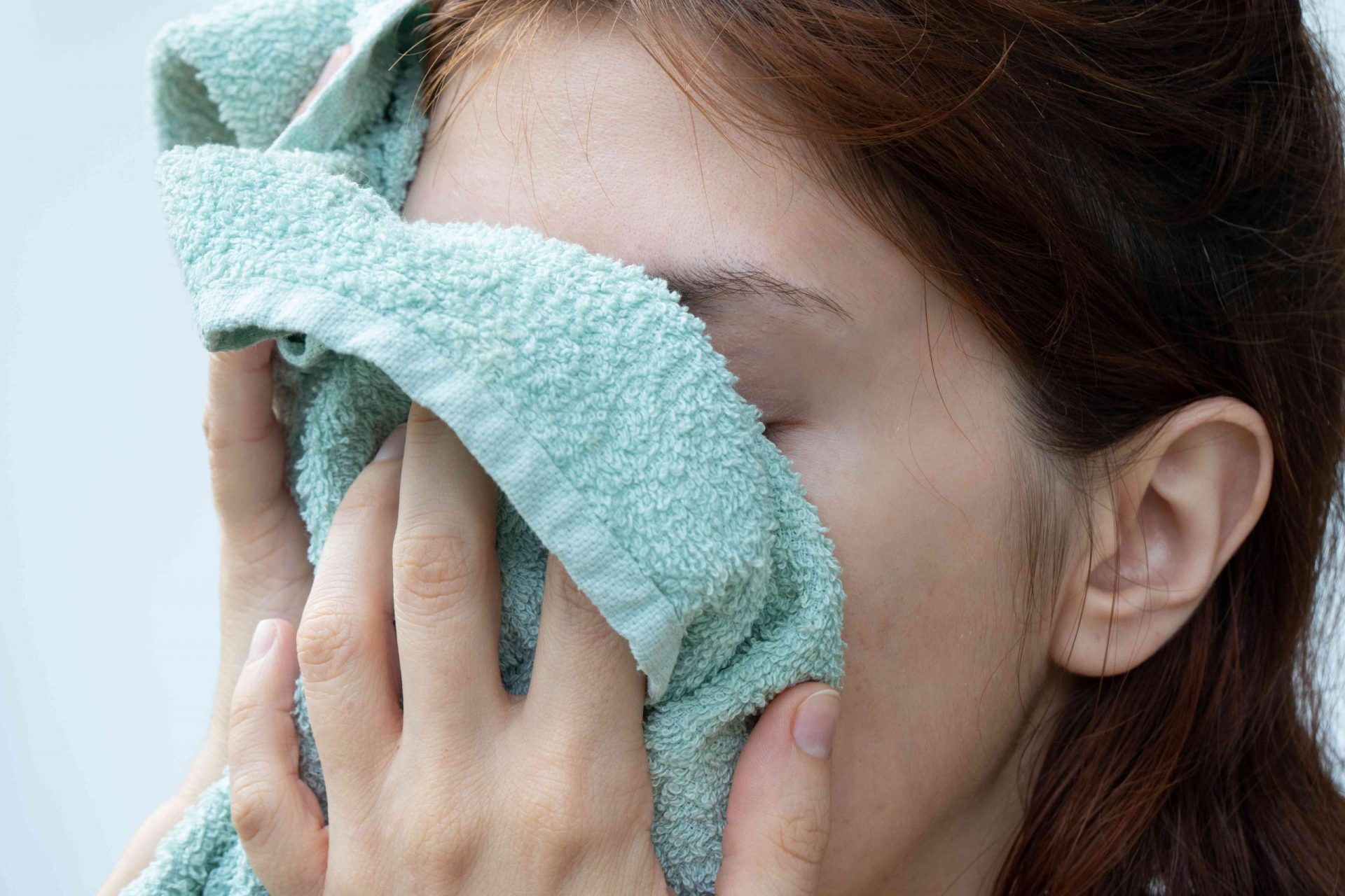 mujer con el pelo oscuro se seca la cara con una toalla de color azul marino