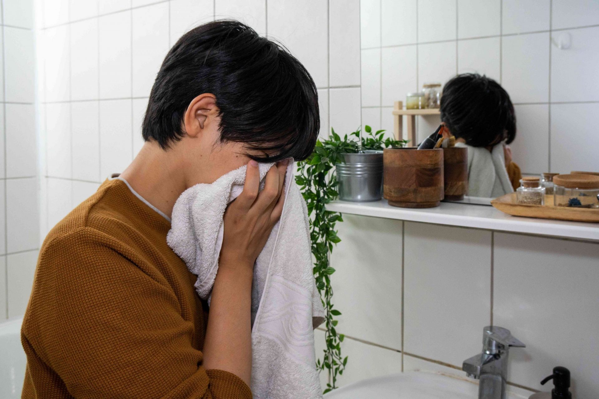 un tipo con jersey marrón se seca la cara con una toalla en el baño
