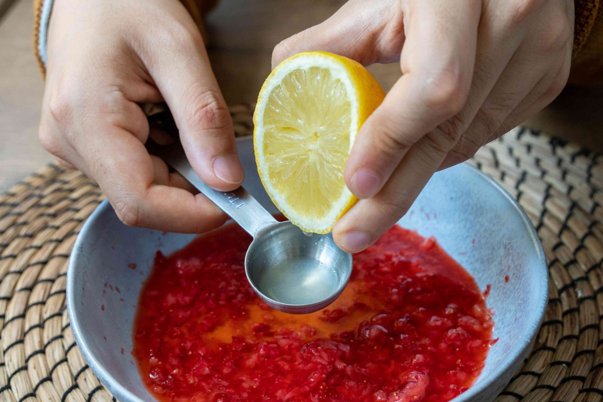 manos exprimir limón cortado en la cuchara medidora sobre el bol de fresas machacadas