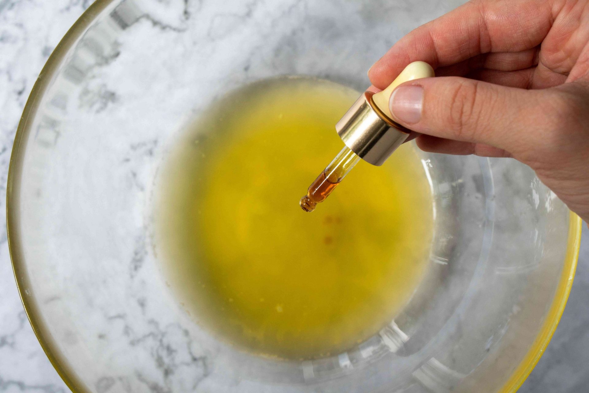 la mano utiliza el cuentagotas para añadir aceites a la manteca de karité derretida en el bol de cristal