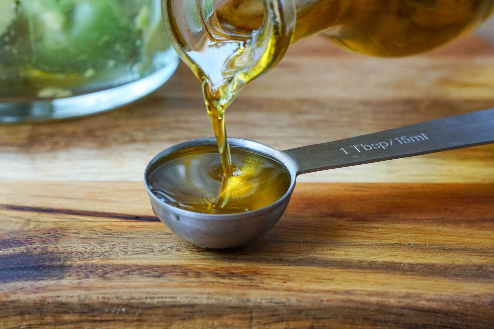 el aceite de oliva de la botella de cristal se vierte lentamente en una cuchara medidora