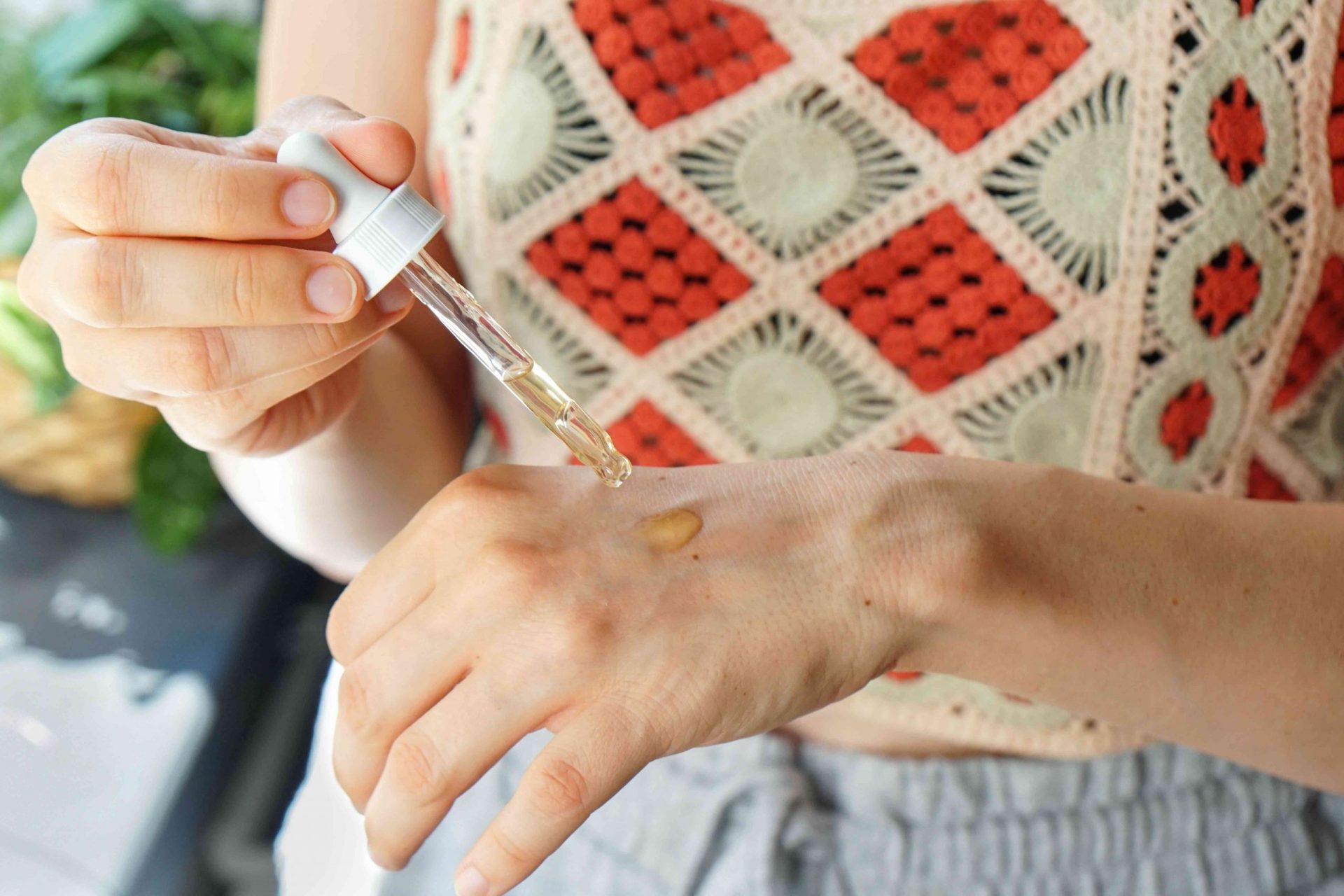una mujer con un top de macramé de punto exprime aceite en la parte superior de la mano con un gotero de cristal