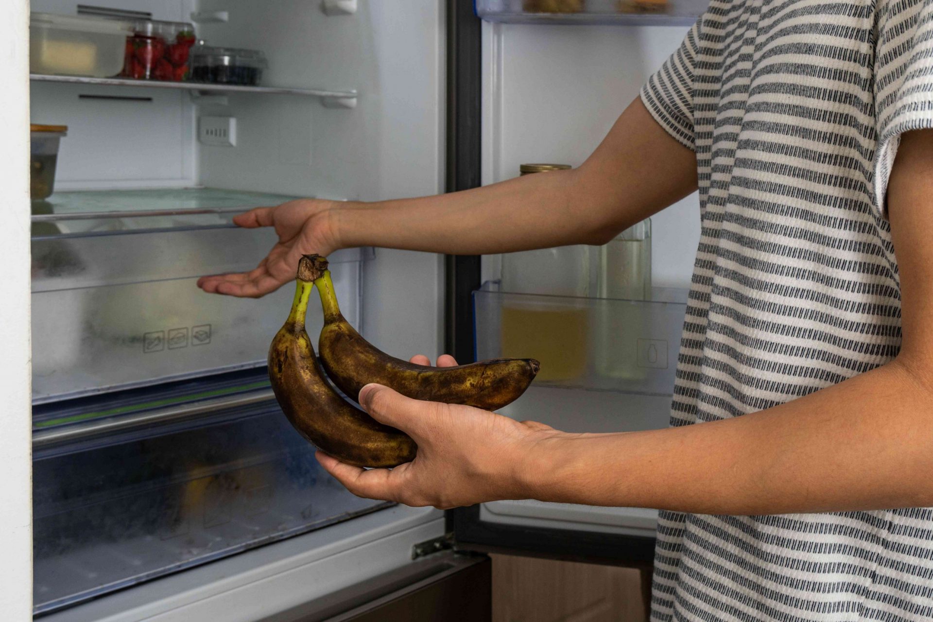 un hombre con camisa de rayas coloca un plátano demasiado maduro en la nevera para esconderse de las moscas
