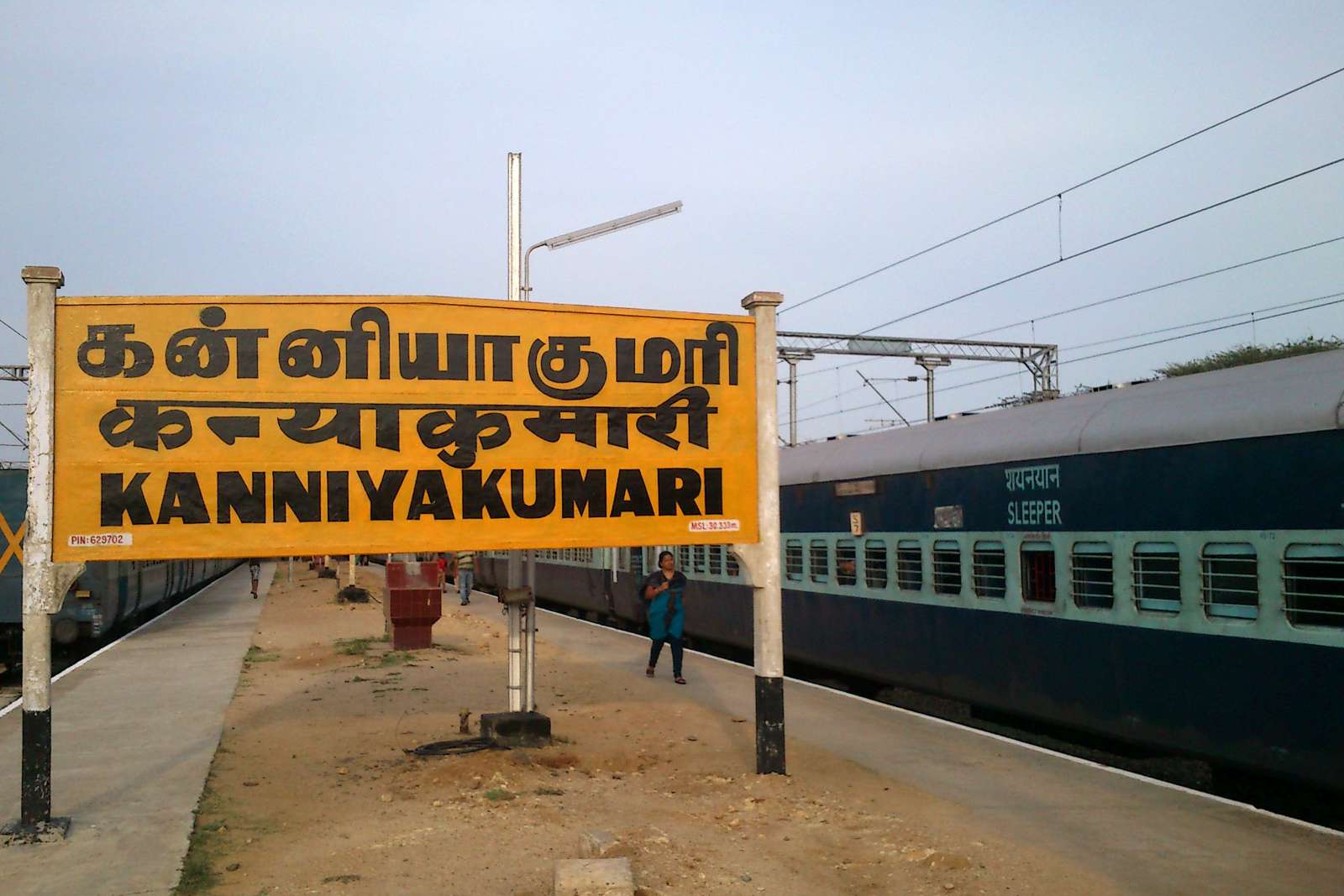 Gran cartel naranja de la estación de tren de Kanyakumari con un tren cama en las vías