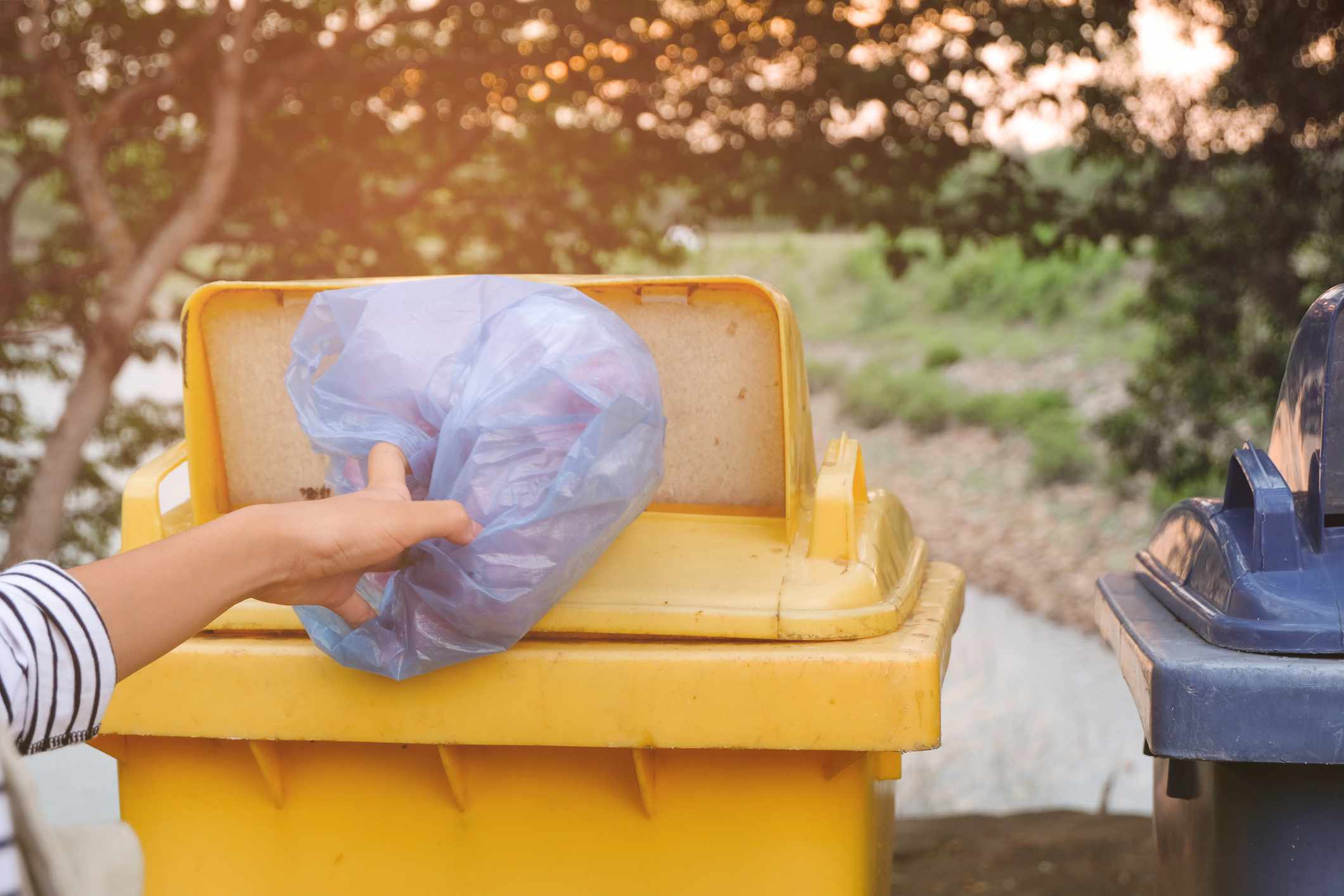 Persona tirando bolsas de plástico en un contenedor amarillo