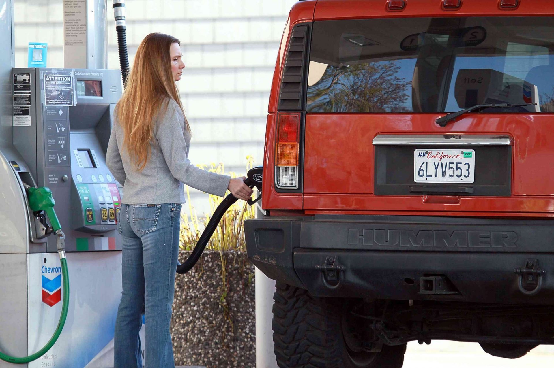Una mujer blanca llenando de gasolina un Hummer rojo