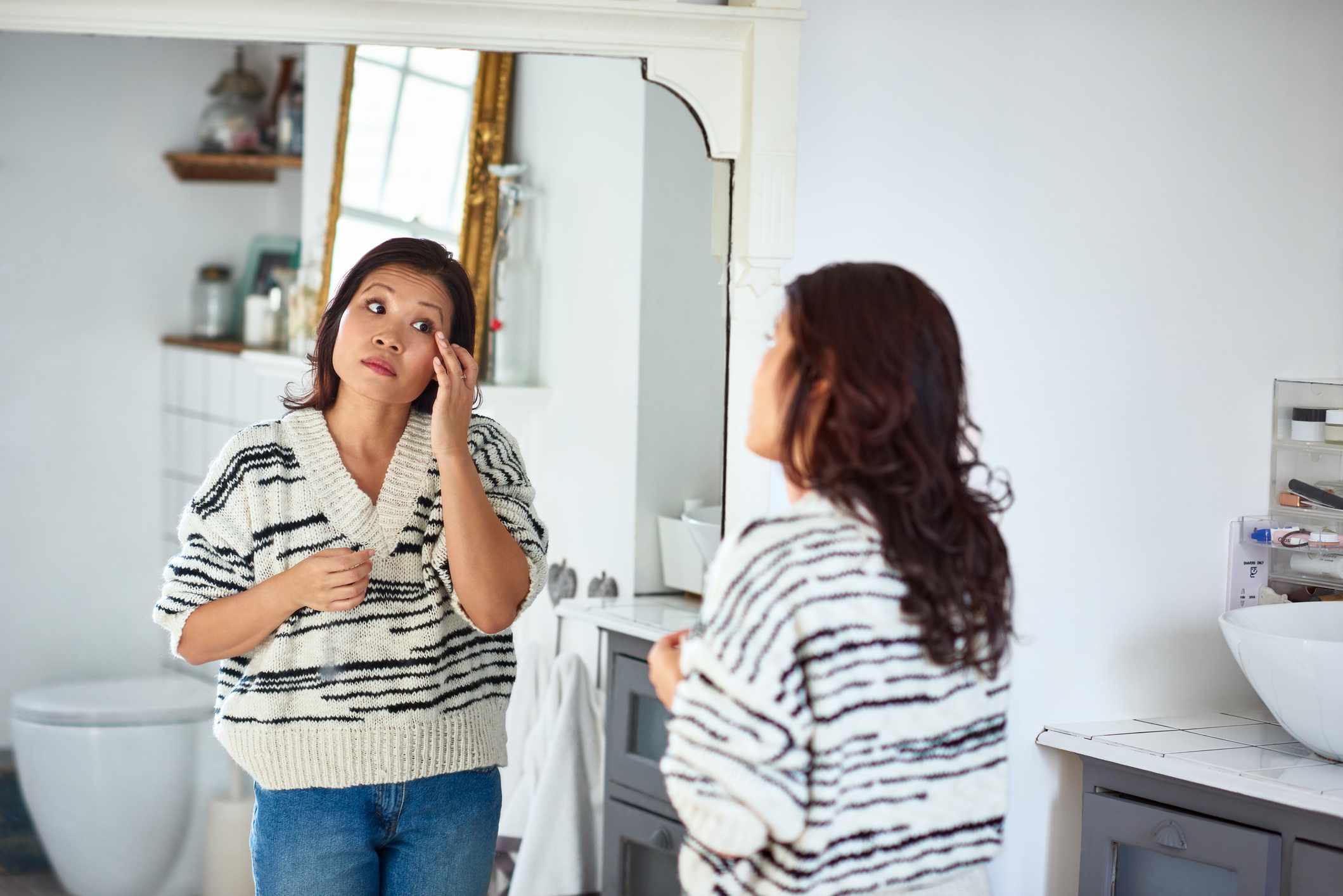 Una mujer asiática con jersey se aplica crema en la cara