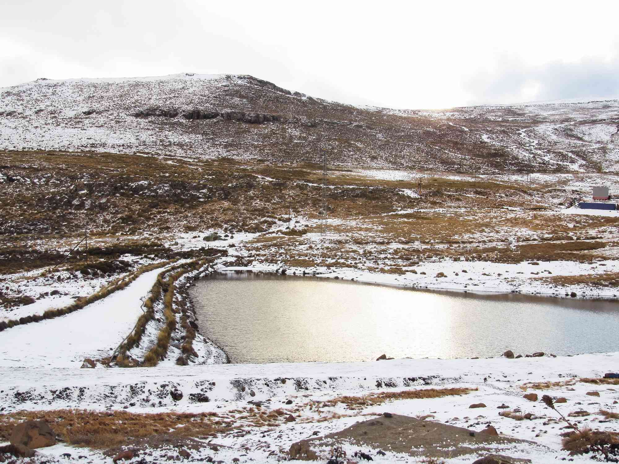 Vista de las montañas de Maluti ligeramente cubiertas de nieve, con partes del marrón crecido por debajo mostrando un lago en el centro durante la temporada de invierno en Lesotho.