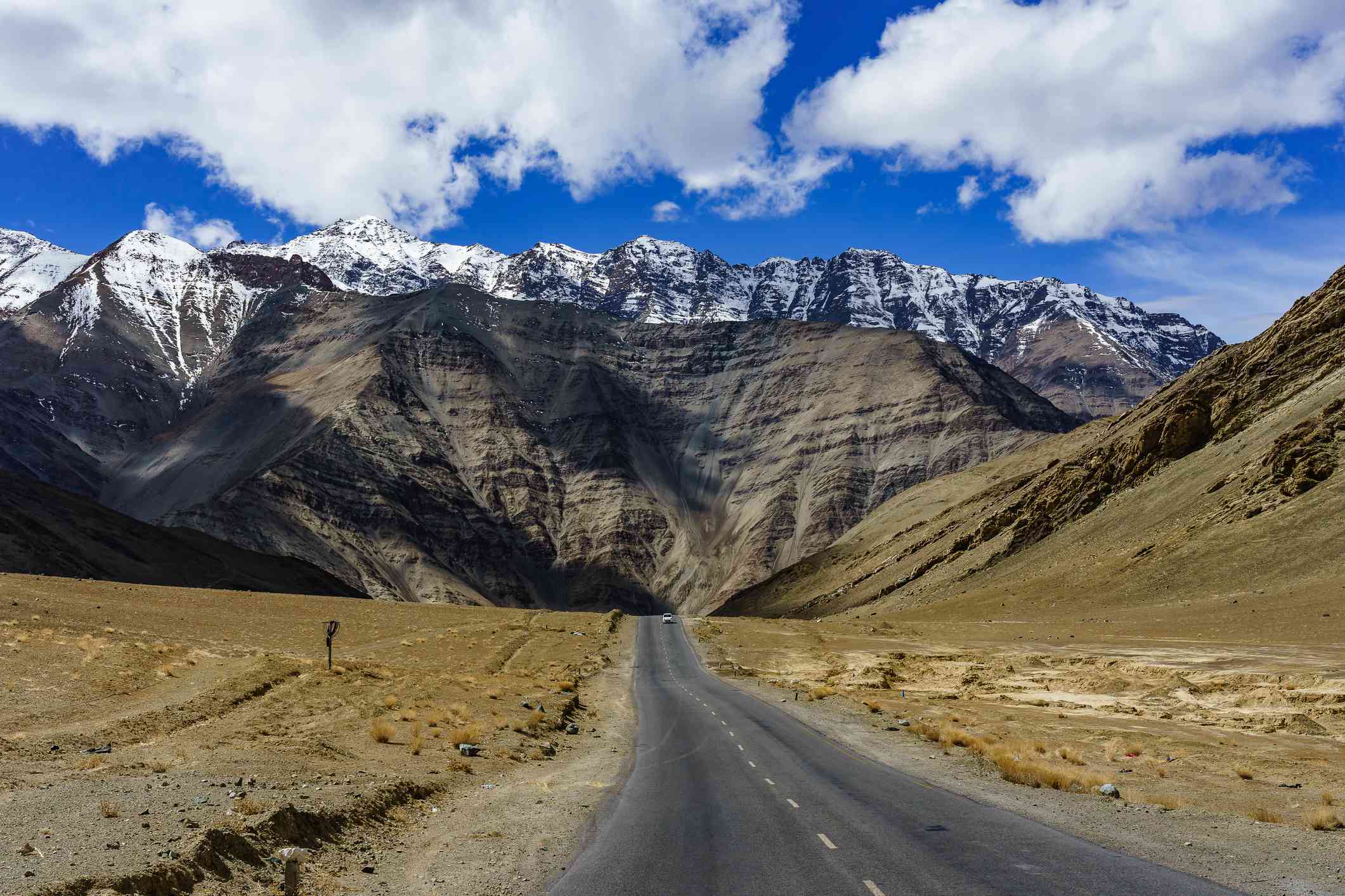 Colina magnética, una colina de gravedad con un coche blanco en la carretera en la distancia en Leh Ladakh, India, con altas montañas nevadas, cielo azul y nubes blancas en la distancia
