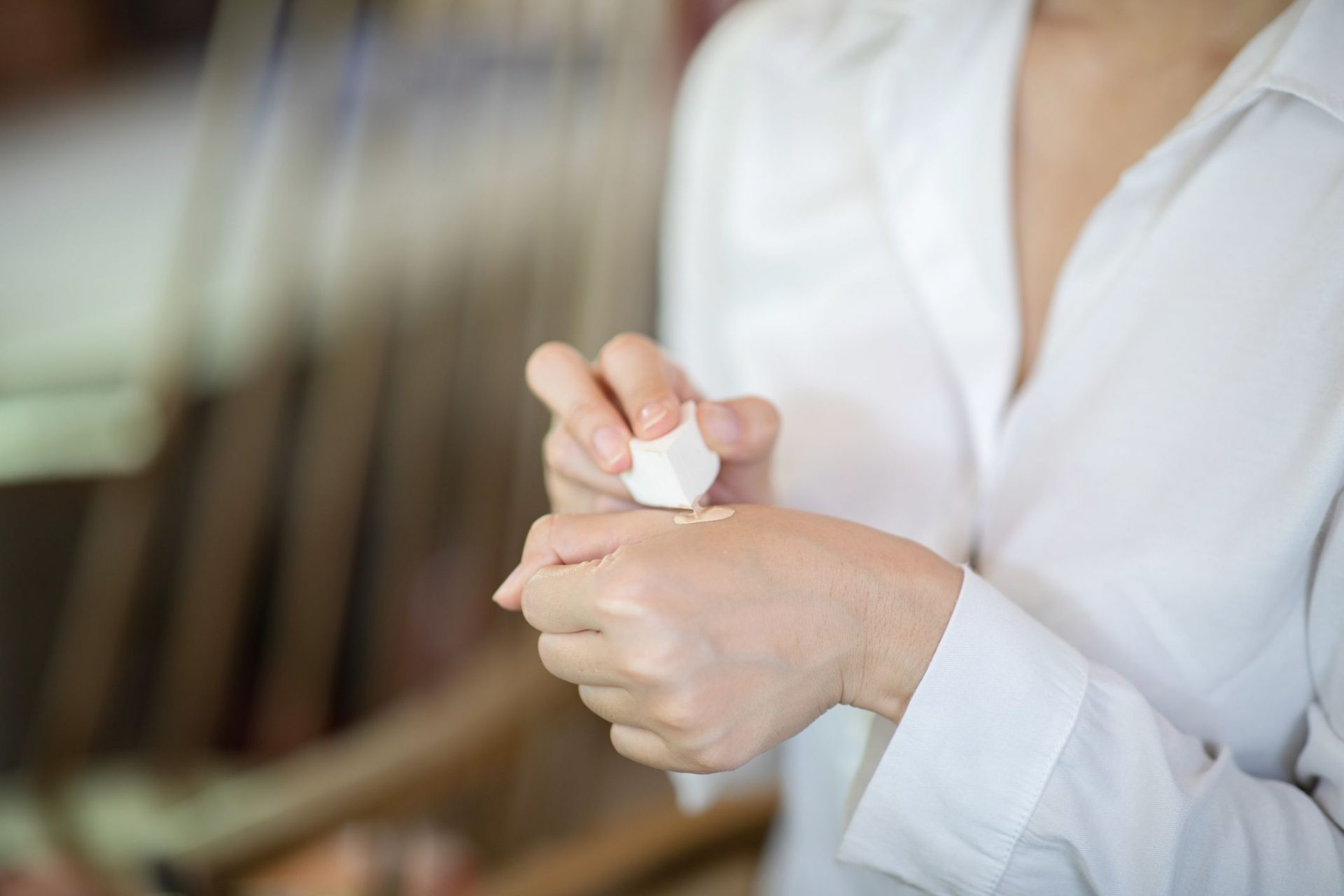 Una mujer con una blusa blanca calienta la base de maquillaje con una esponja en la mano