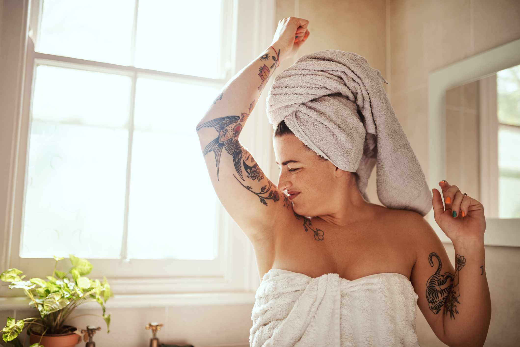 Una mujer blanca con tatuajes oliendo sus axilas en el lavabo