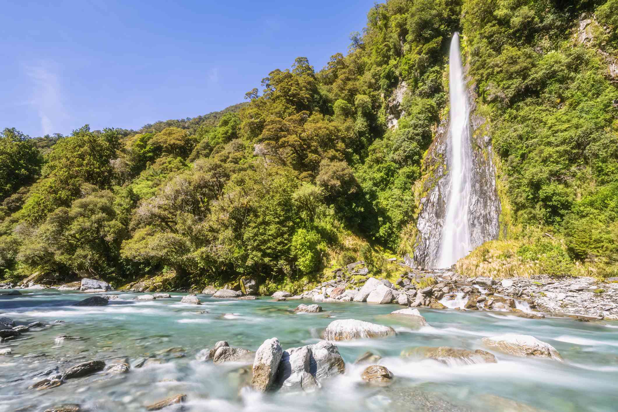 La cascada de Thunder Creek Falls vierte agua desde una montaña cubierta de árboles a un estanque de agua verde lleno de formaciones rocosas
