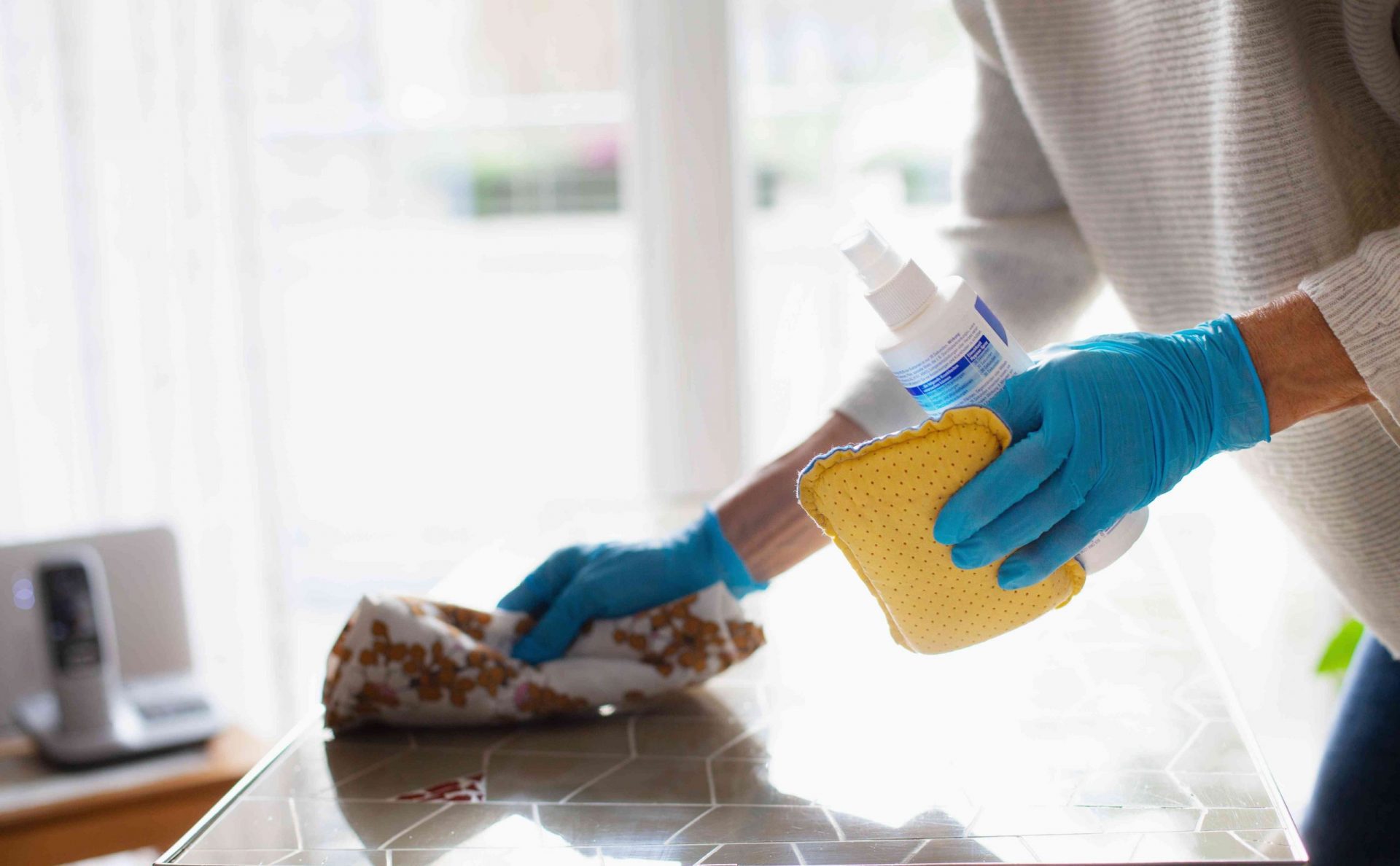 Una persona con guantes de goma y una botella y esponja limpia una encimera